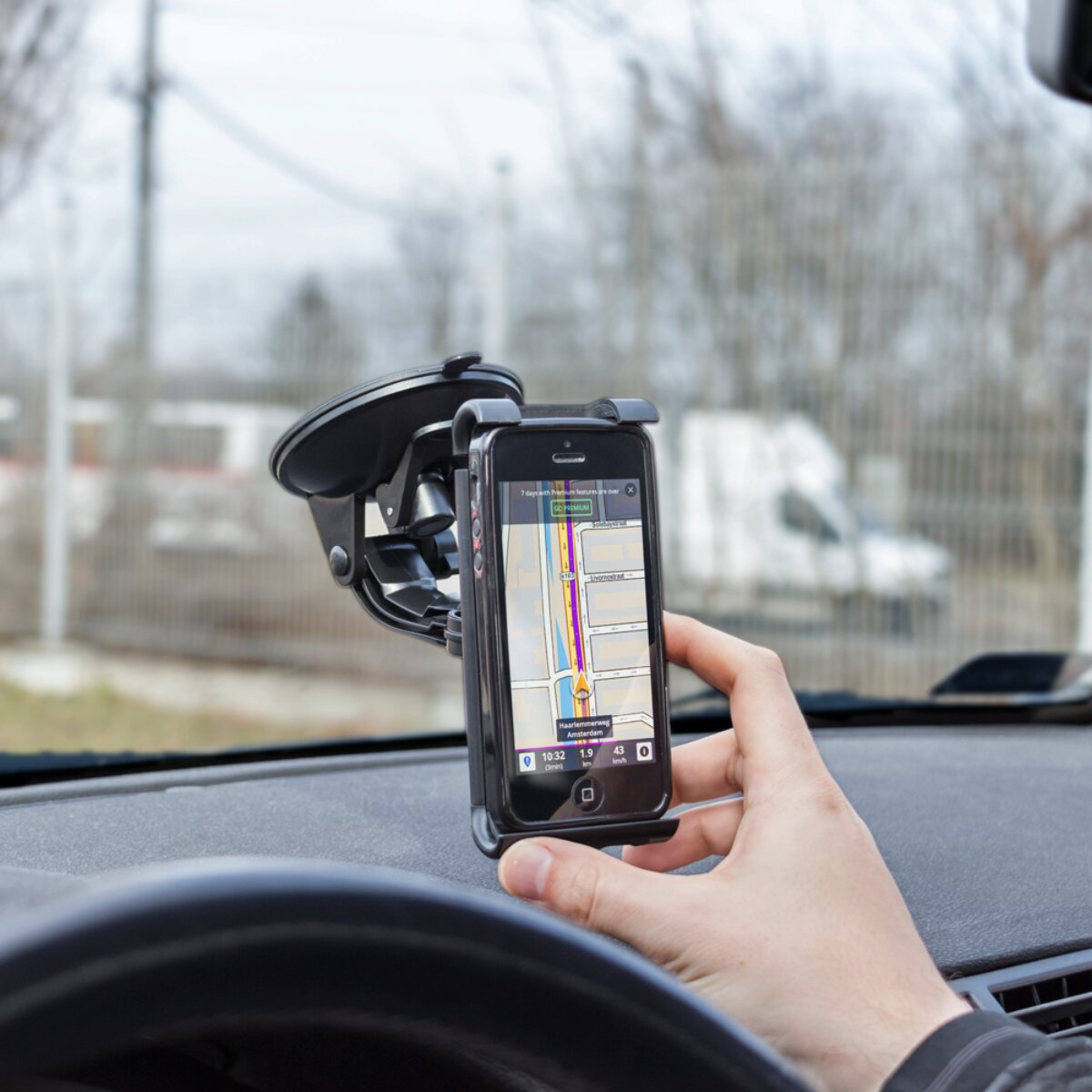 Una mano tiene uno smartphone in un supporto per auto con mappa, su sfondo sfocato.