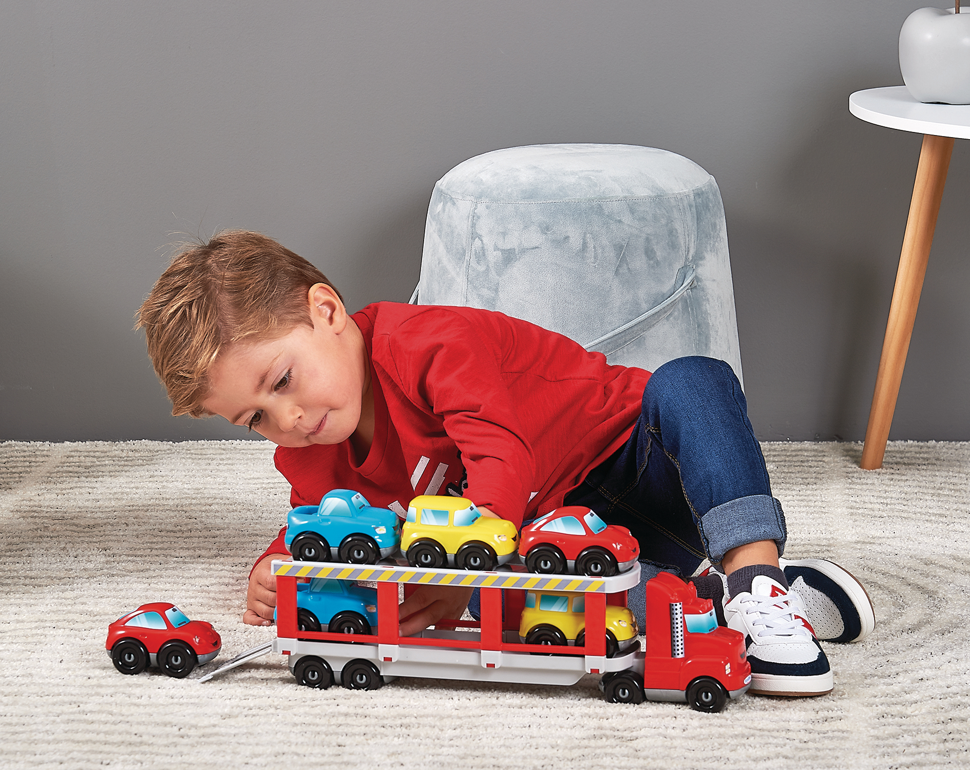 Junge spielt auf Teppich mit rotem Auto-Transporter und bunten Spielzeugautos.