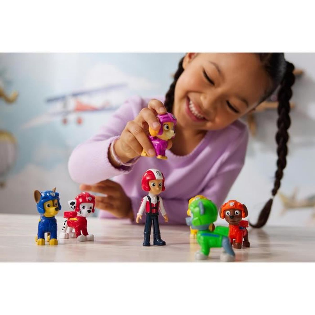 Ein smiling Mädchen spielt mit PAW Patrol Figuren auf einem Tisch.