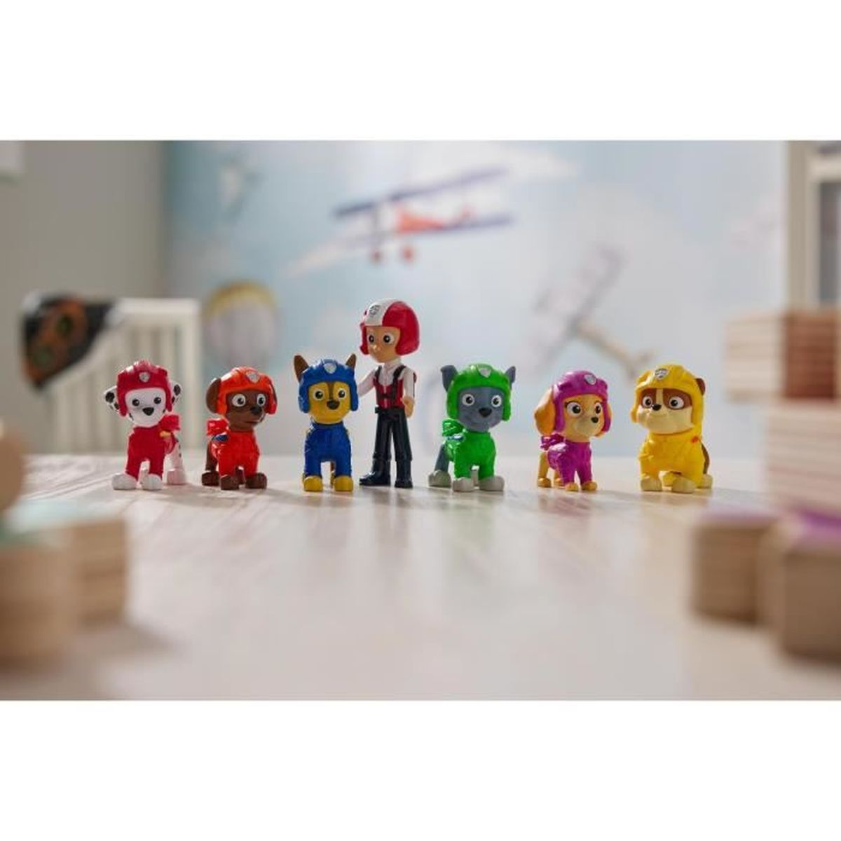 Sechs Paw Patrol Figuren und Ryder stehen auf einem Tisch in einem Kinderzimmer.