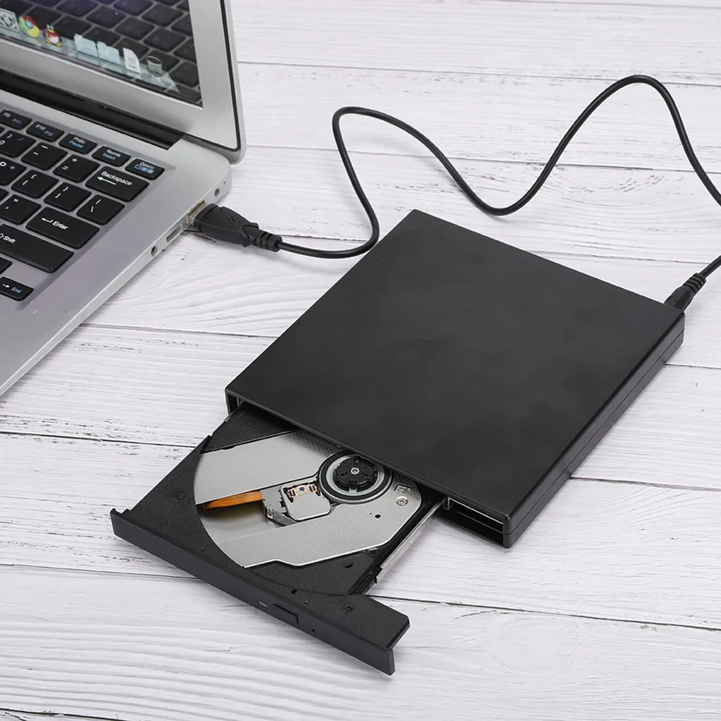 Ein schwarzes externes DVD-Laufwerk ist per USB-Kabel an einen Laptop angeschlossen, auf einem Holztisch.