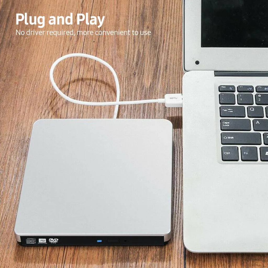 Ein silbernes externes DVD-Laufwerk ist per USB-Kabel an einen Laptop auf einem Holztisch angeschlossen.