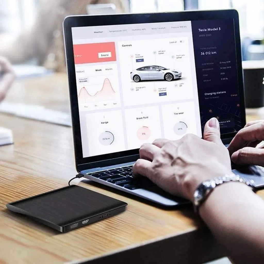 Person tippt auf Laptop mit Auto-App auf dem Bildschirm; externer DVD-Player auf dem Holztisch.