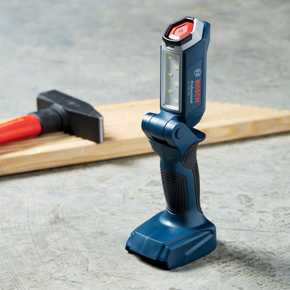 Eine blaue Bosch Akku-Arbeitsleuchte steht auf Beton, im Hintergrund ein Holzbrett und ein Hammer.