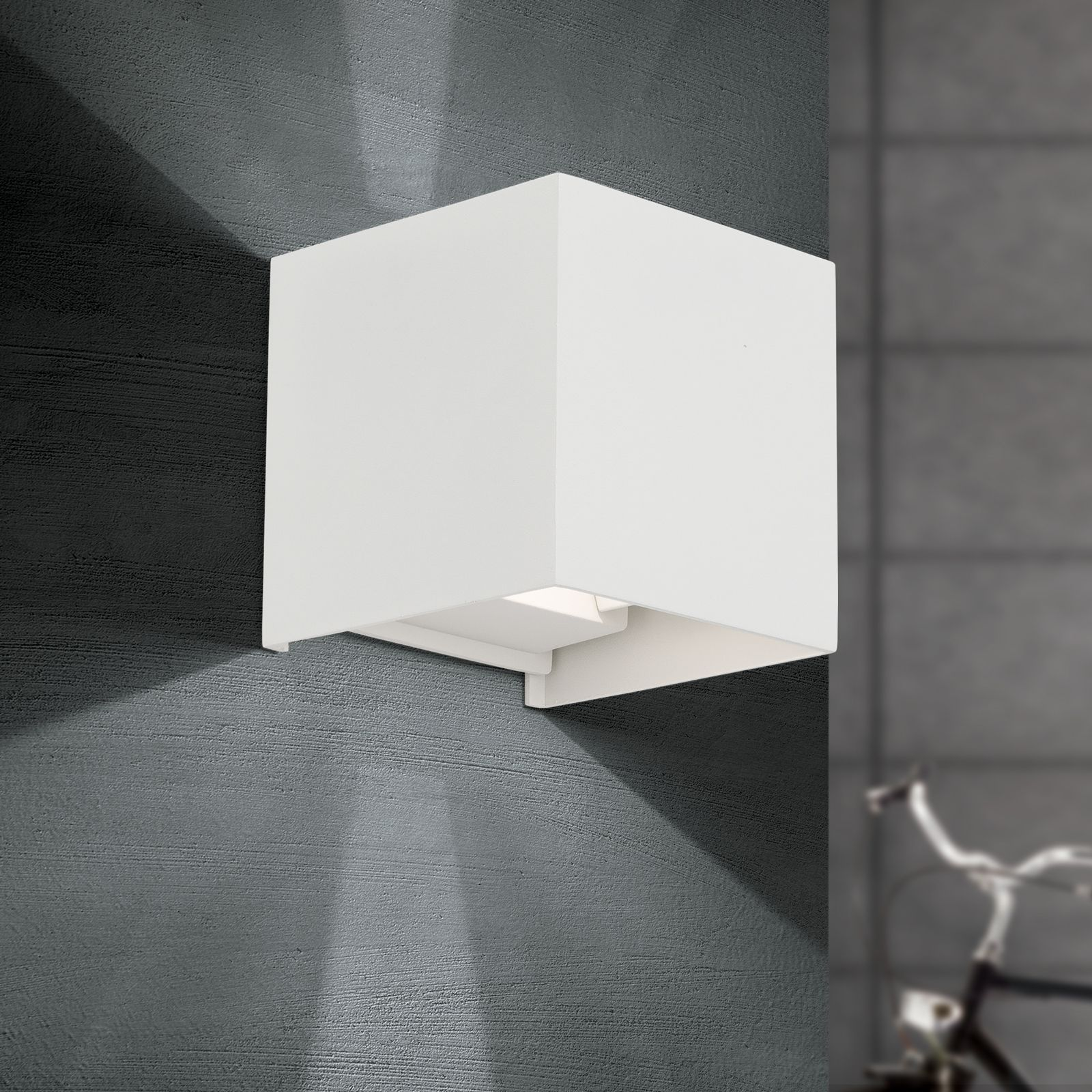 Eine weiße quaderförmige Wandleuchte an einer dunklen Wand wirft Licht nach oben und unten.