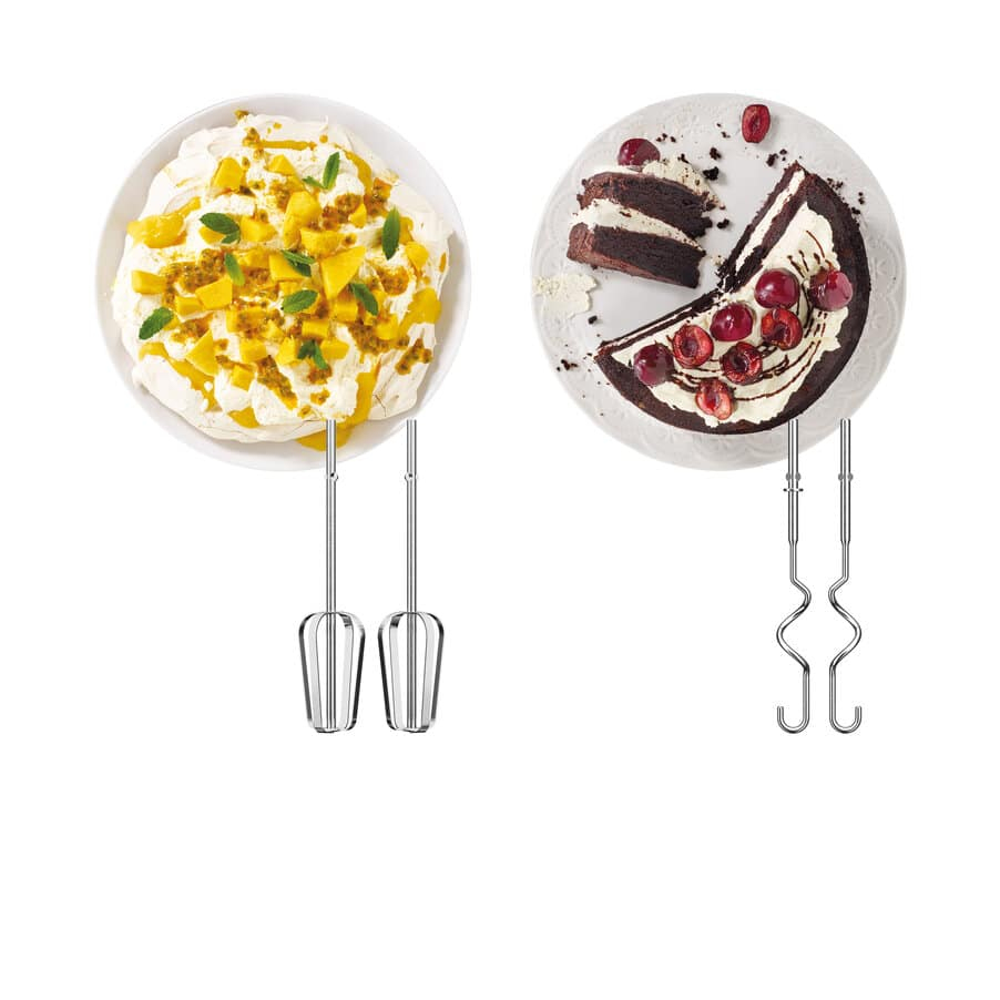 Due piatti di dolci: a sinistra pavlova al mango, a destra torta al cioccolato e ciliegie, con fruste da cucina.
