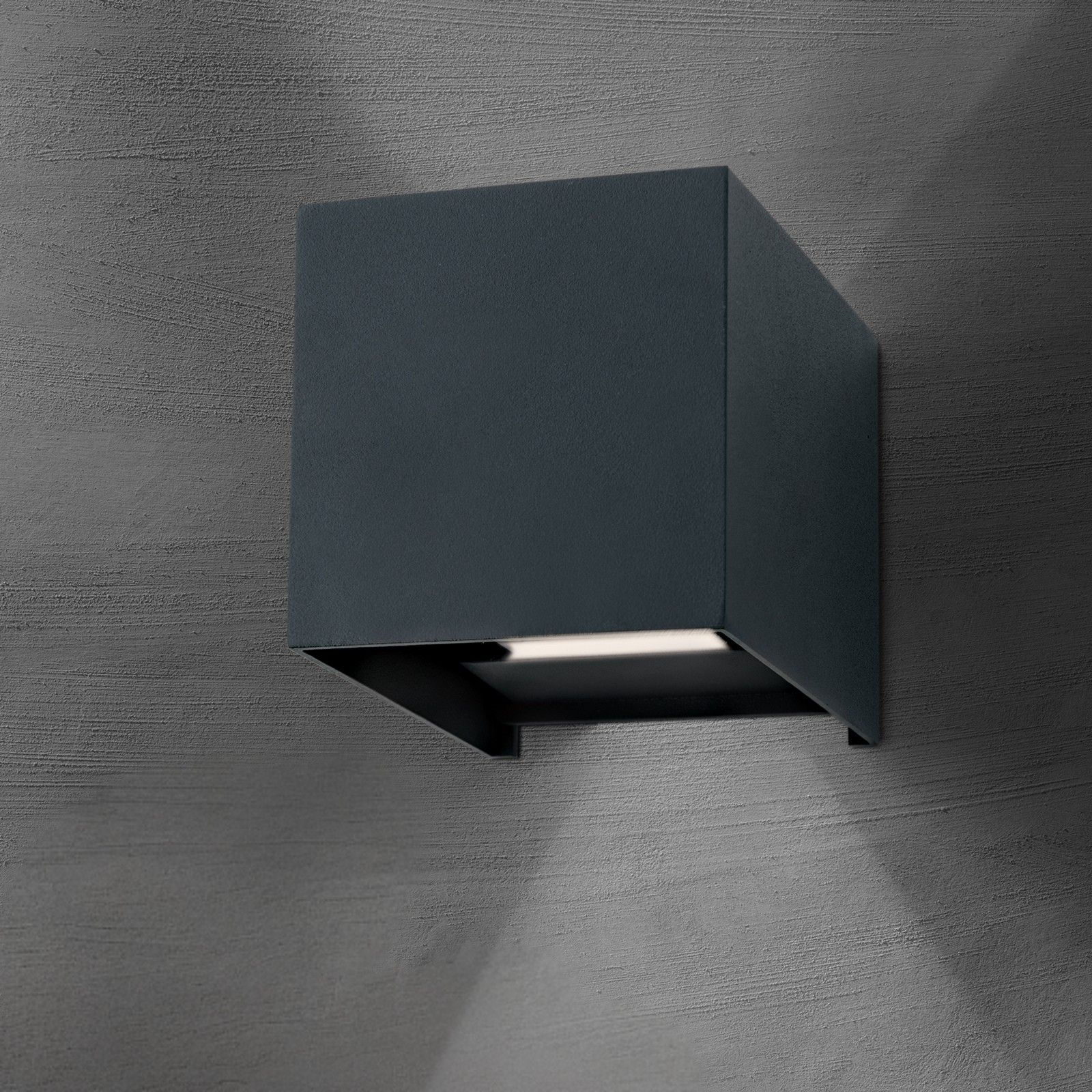 Eine schwarze, kubische Wandleuchte ist an einer grauen, strukturierten Wand montiert und wirft Licht nach unten.