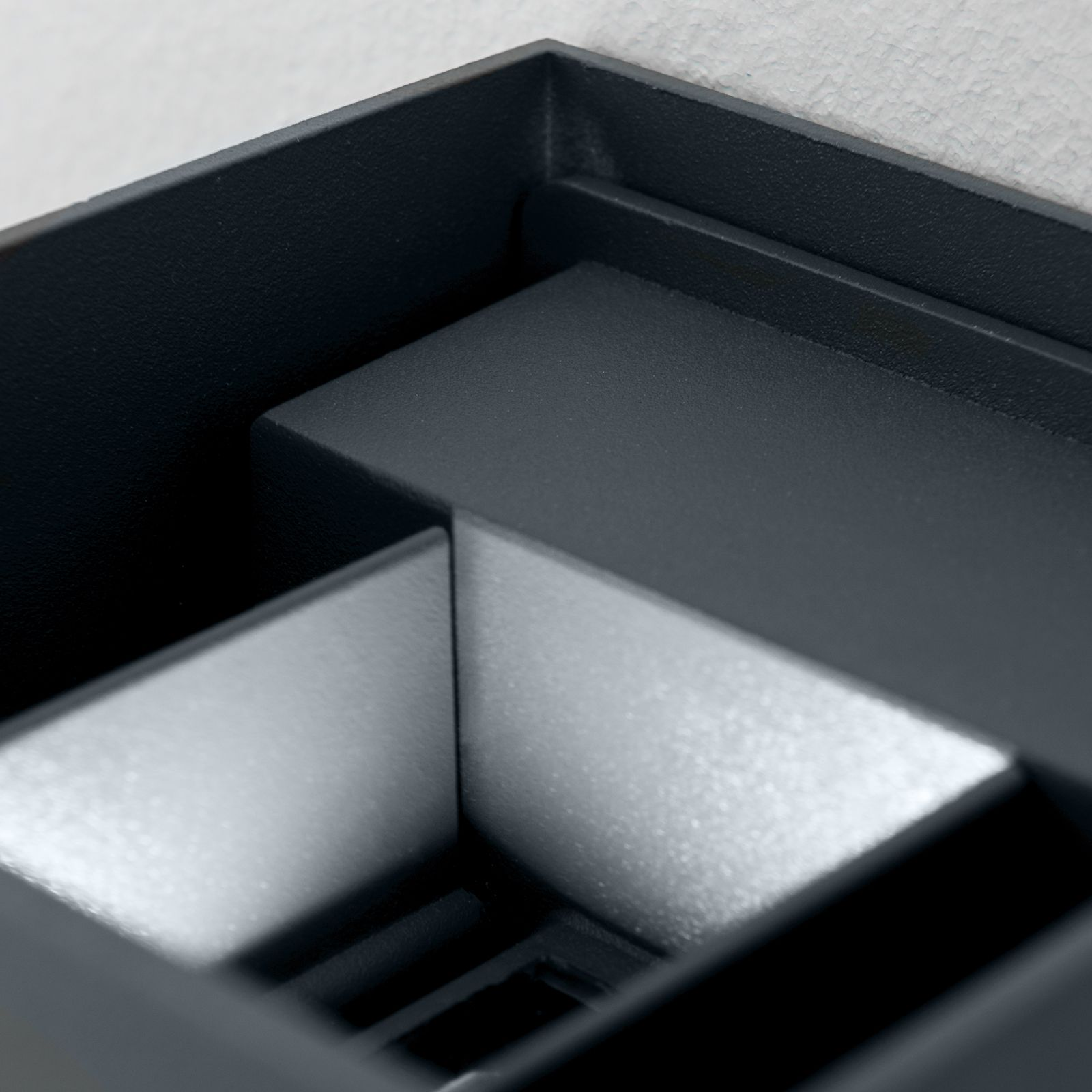 Nahaufnahme einer dunklen, geometrischen Lampe mit silbernem Innenbereich an einer weißen Wand.