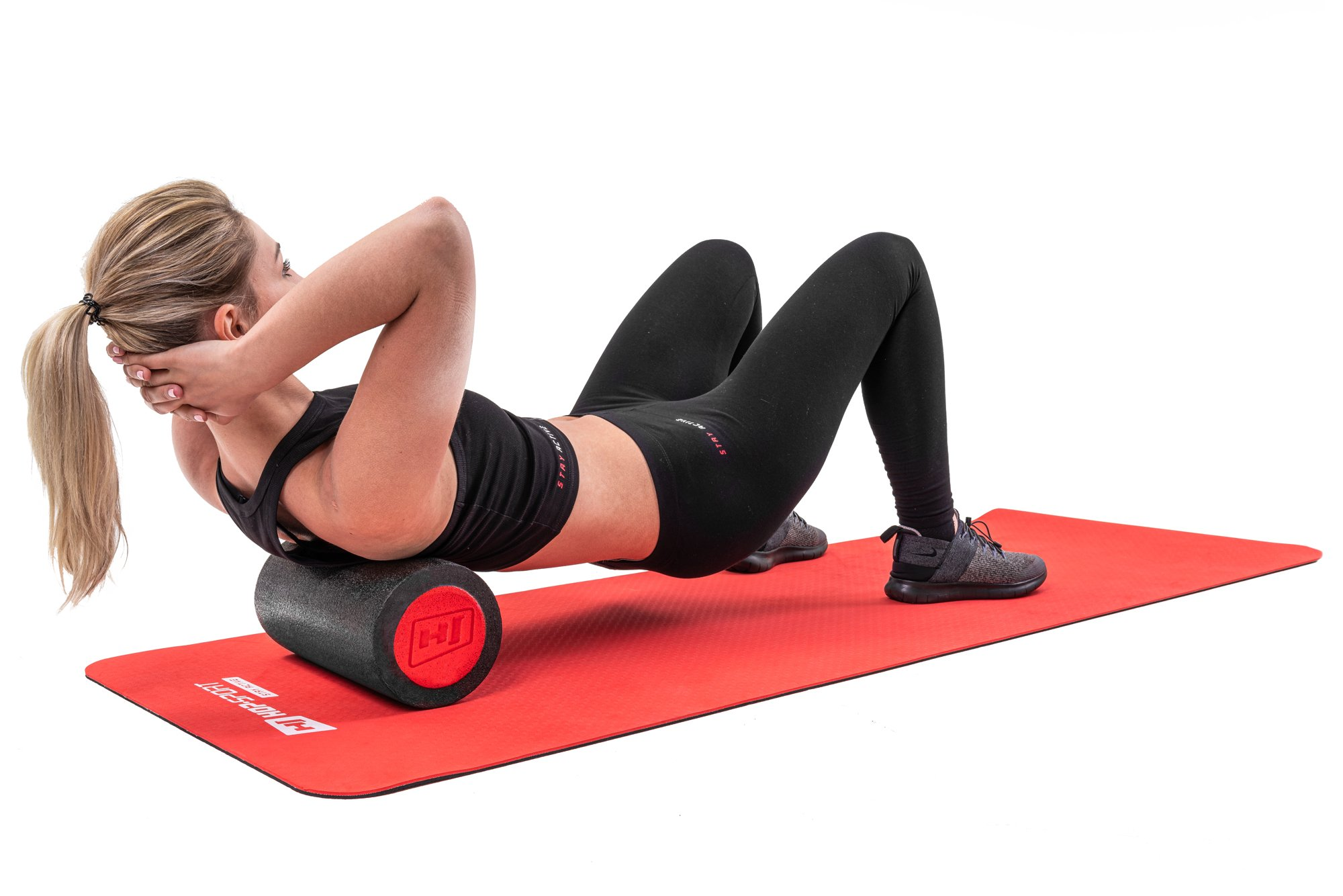 Frau in schwarzem Sportoutfit nutzt eine schwarze Faszienrolle mit roten Enden auf einer roten Yogamatte.