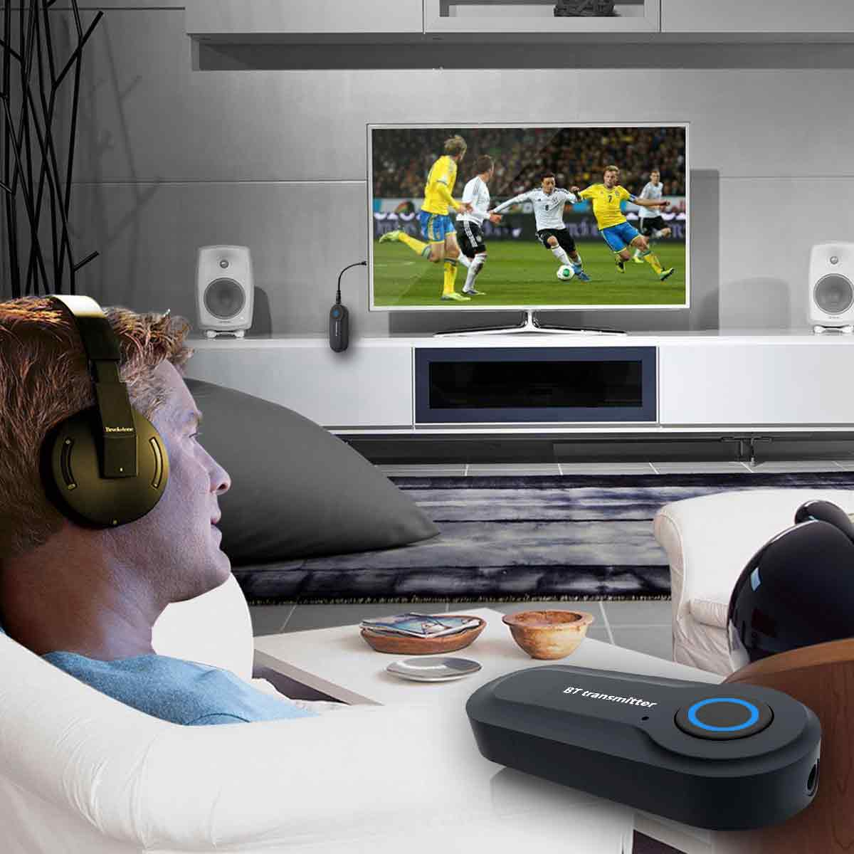Ein Mann sitzt mit Kopfhörern im Wohnzimmer und schaut Fußball auf dem Fernseher.