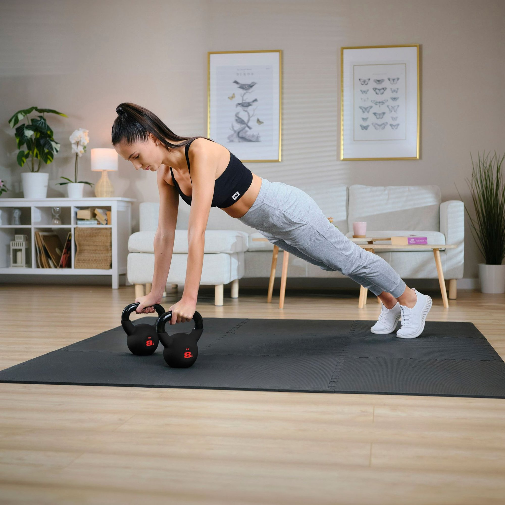 Eine Frau macht im Wohnzimmer Liegestütze auf zwei Kettlebells und einer schwarzen Matte.