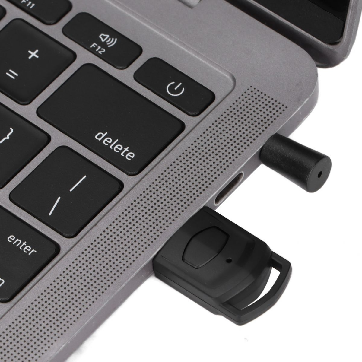 Ein schwarzer USB-Empfänger und ein Stylus stecken in den Anschlüssen eines grauen Laptops.