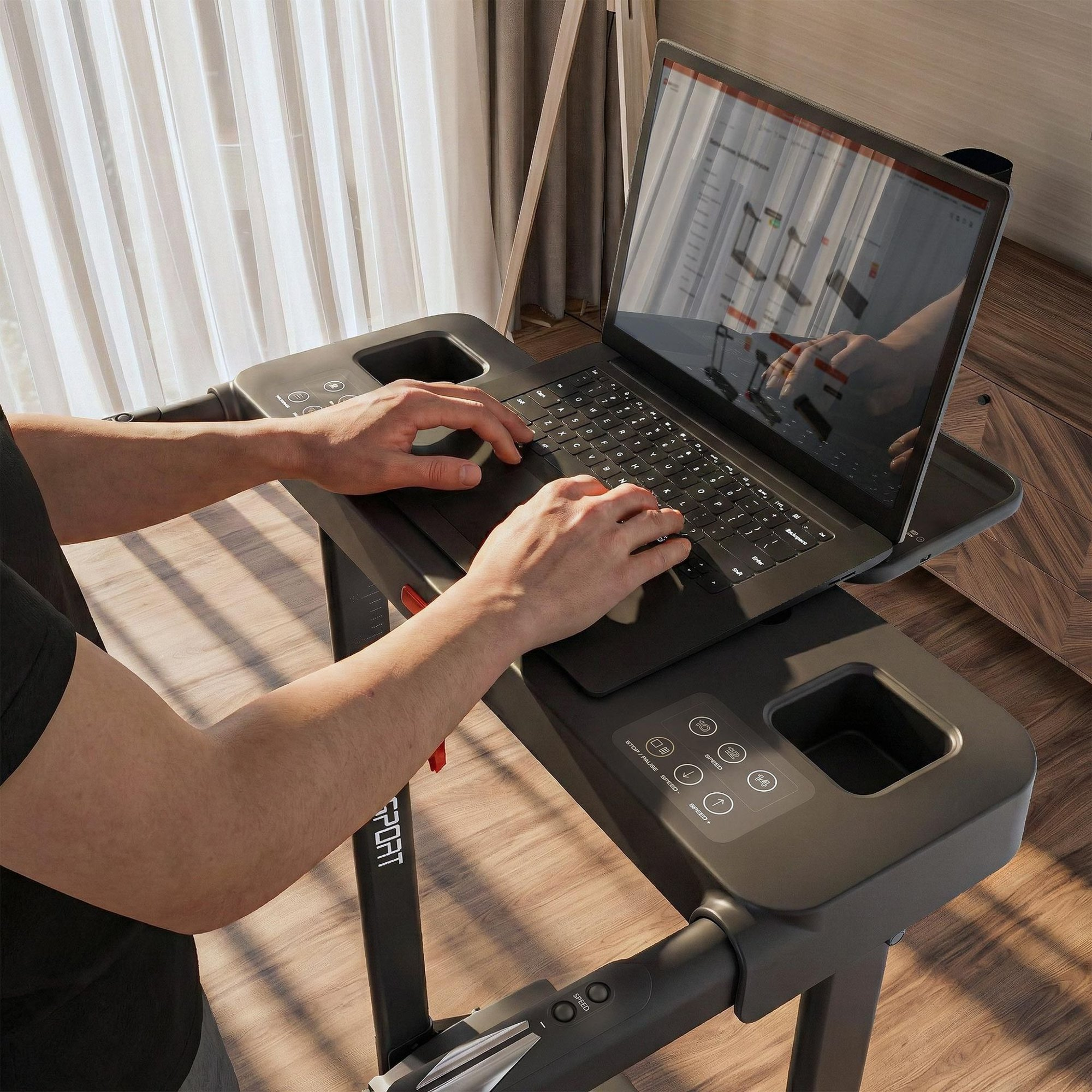 Ein Mann tippt auf einem Laptop, der auf einem Laufband-Schreibtisch in einem sonnigen Raum steht.