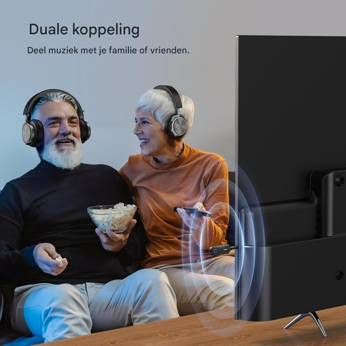 Ein älteres Paar mit Kopfhörern sitzt auf dem Sofa und sieht fern, während es Popcorn und eine Fernbedienung hält.