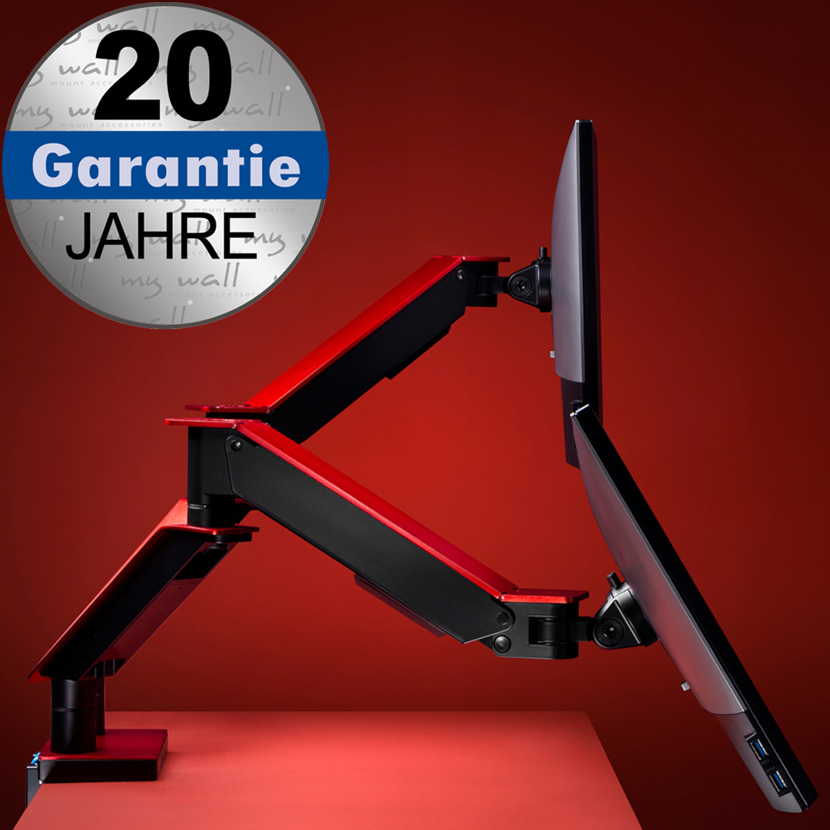 Ein rot-schwarzer Doppelmonitorarm auf einem roten Tisch mit einem runden Aufkleber für 20 Jahre Garantie.