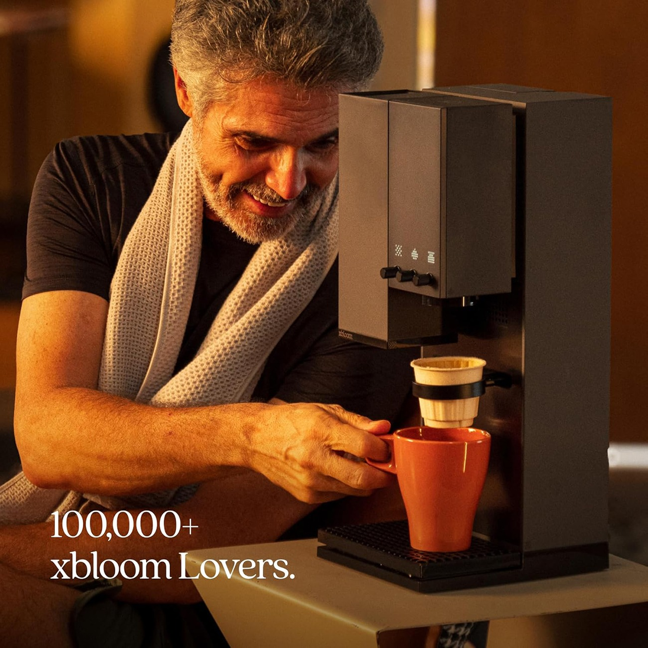 Ein Mann mit Handtuch um den Hals stellt eine orange Tasse unter eine schwarze Kaffeemaschine.