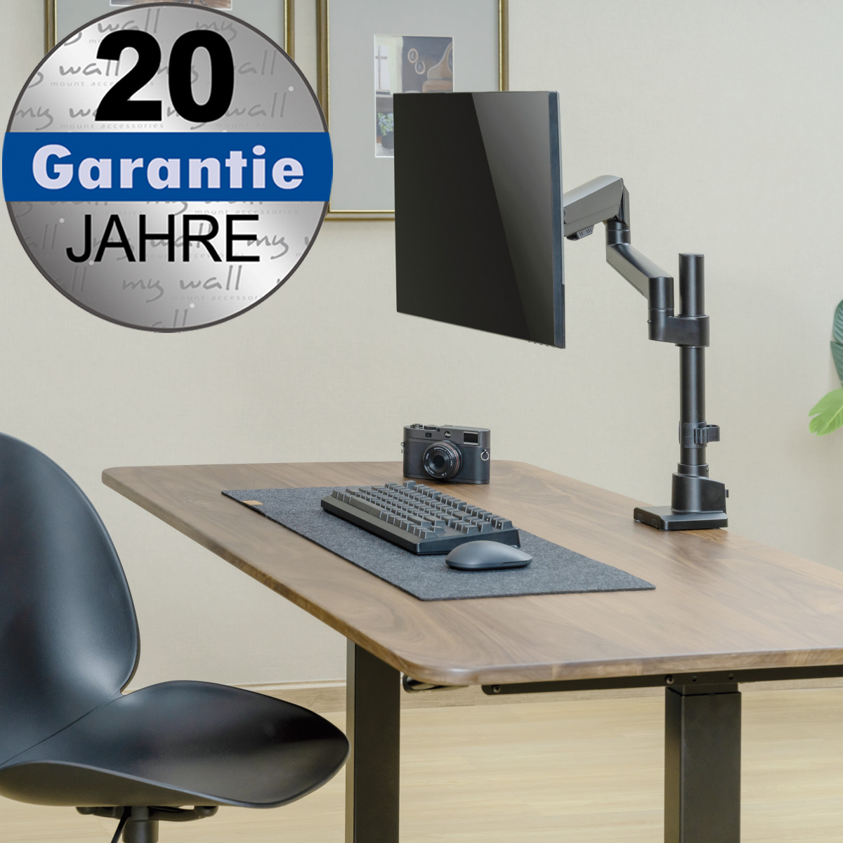 Ein Monitorarm auf einem Holztisch mit Tastatur, Maus und Kamera. Oben links ein 20-Jahre-Garantie-Symbol.