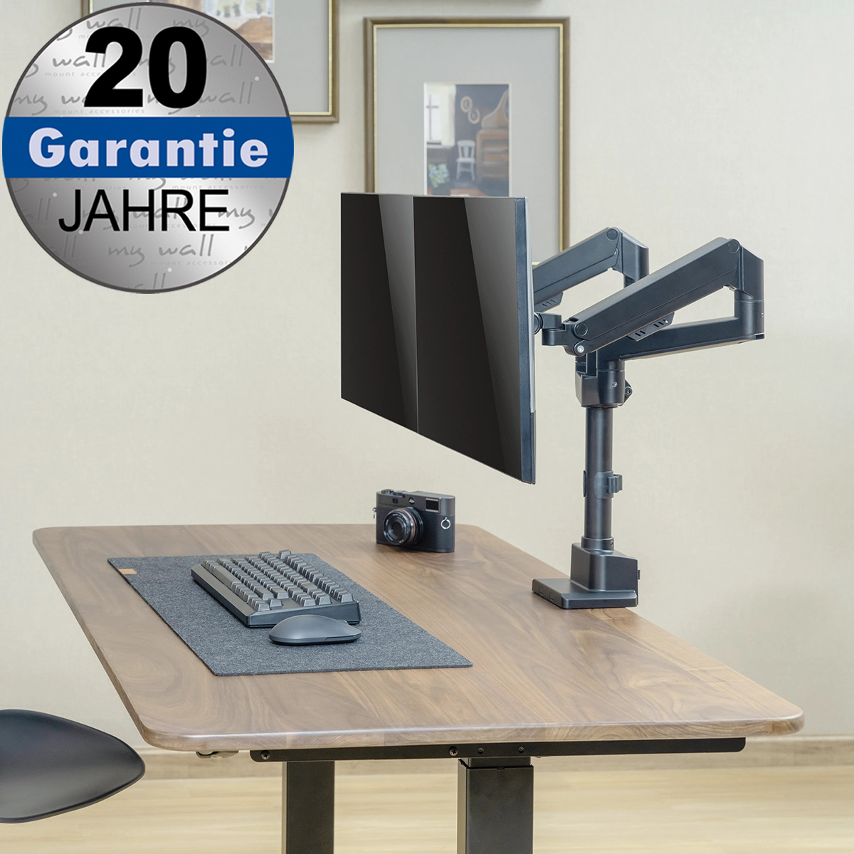 Ein Schreibtisch mit Monitorarm, Tastatur, Maus und Kamera. Oben links ein Garantieschild.