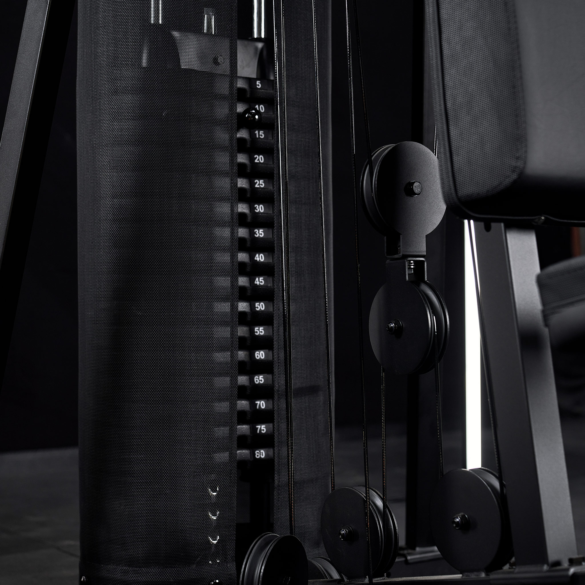 Ein schwarzer Kraftturm mit Gewichtsplatten, Riemenscheiben und Seilen in einem Fitnessstudio.