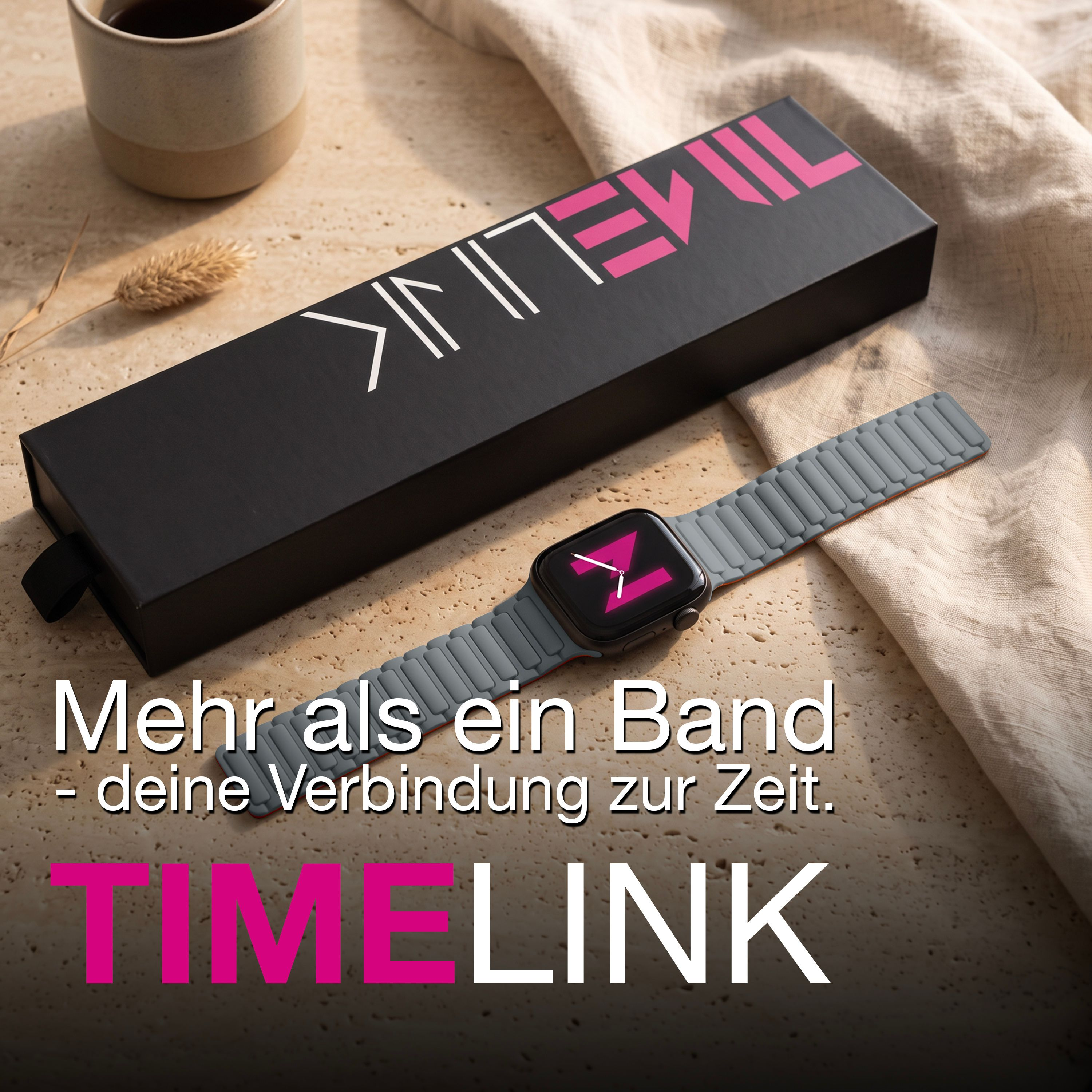 Eine Smartwatch mit grauem Band liegt neben einer schwarzen Box und einer Tasse auf sandfarbenem Untergrund.