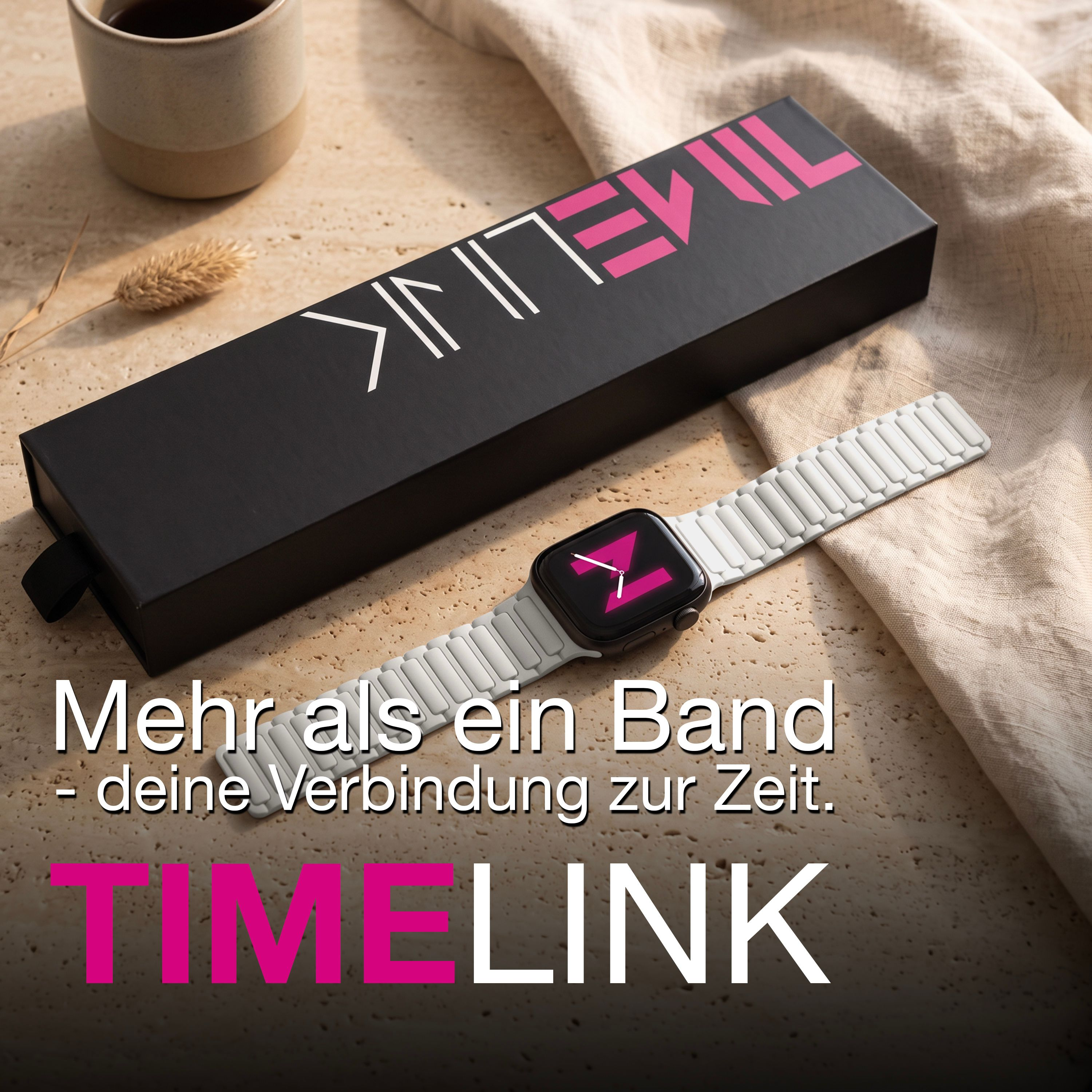 Eine Smartwatch mit weißem Armband liegt neben einer schwarzen Box und einer Tasse auf einem Stofftisch.