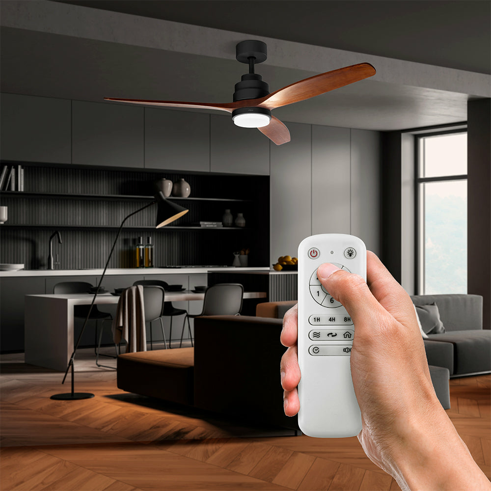 Una mano tiene un telecomando bianco, con un moderno ventilatore da soffitto, cucina e soggiorno sullo sfondo.