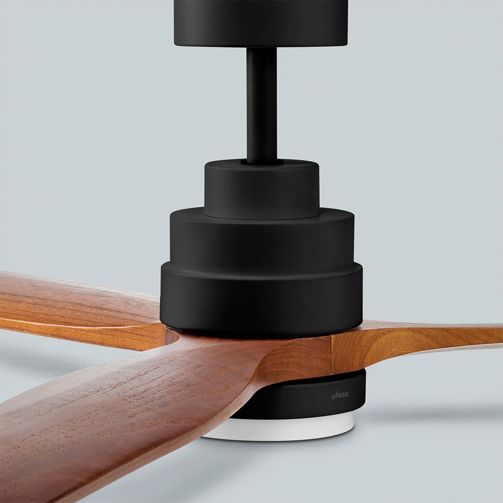Un ventilatore da soffitto con supporti neri e tre pale in legno su sfondo chiaro.