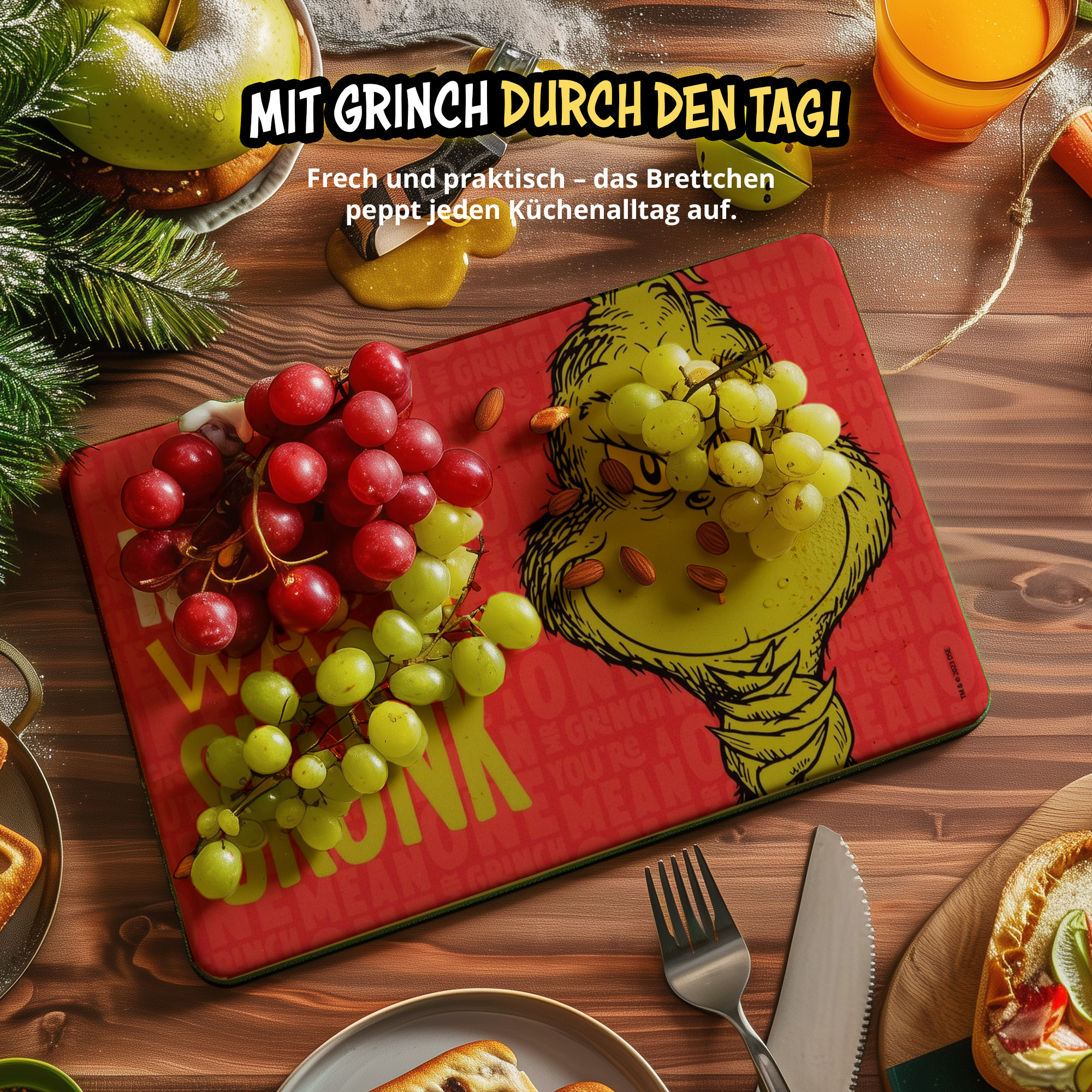 Ein rotes Schneidebrett mit dem Grinch, belegt mit roten und grünen Trauben, auf einem Holztisch.