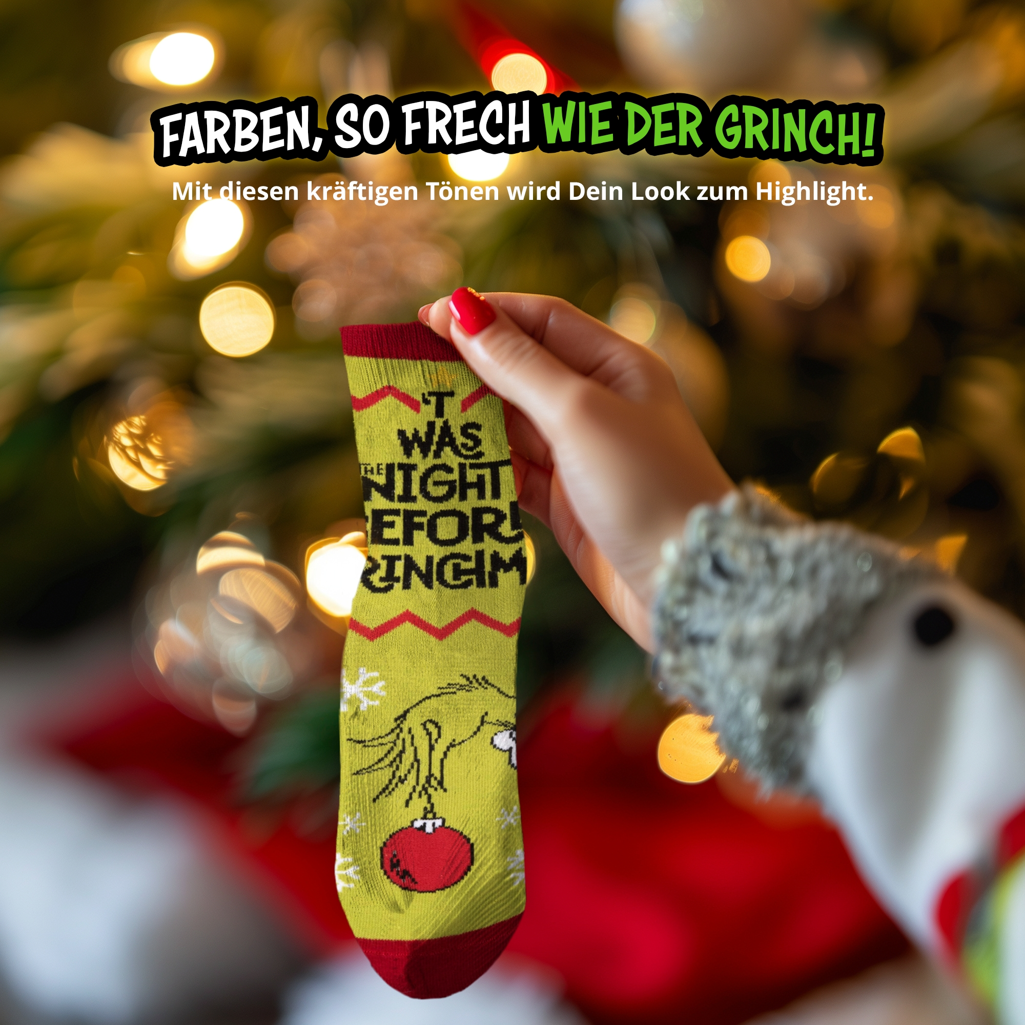 Eine Hand hält eine gelbe Grinch-Weihnachtssocke mit Text und roten Akzenten vor einem Baum.
