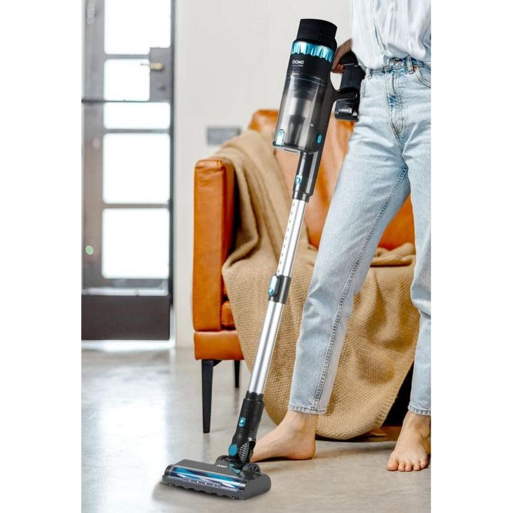 Person in Jeans verwendet einen schwarzen und silbernen Akkusauger vor einem Ledersofa.