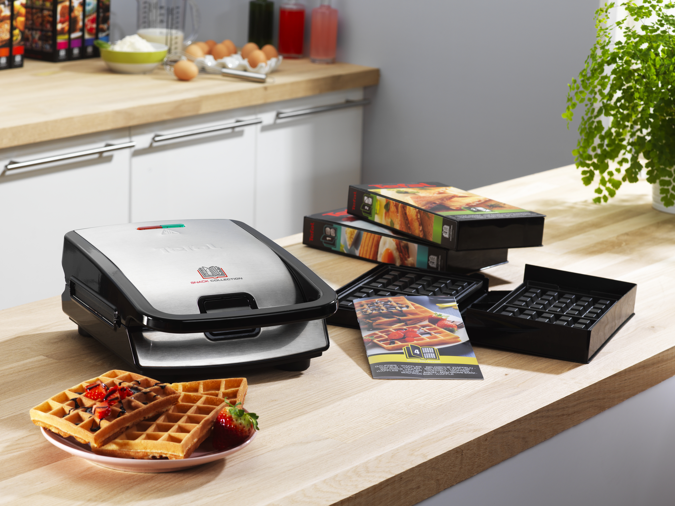 Una piastra per waffle su un piano di lavoro in legno, con waffle freschi, fragole e accessori.