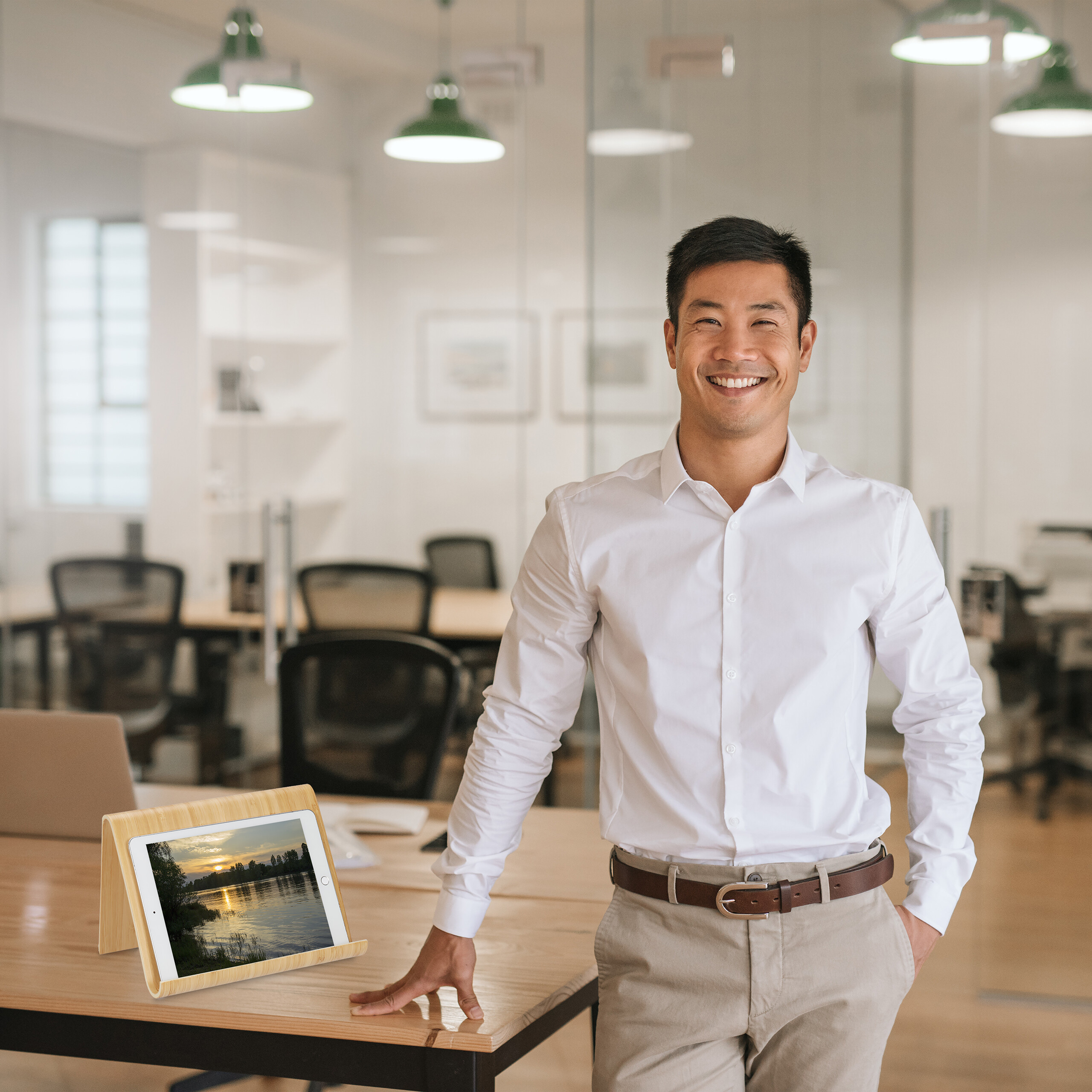 Lächelnter asiatischer Geschäftsmann steht im modernen Büro am Holztisch mit Tablet.