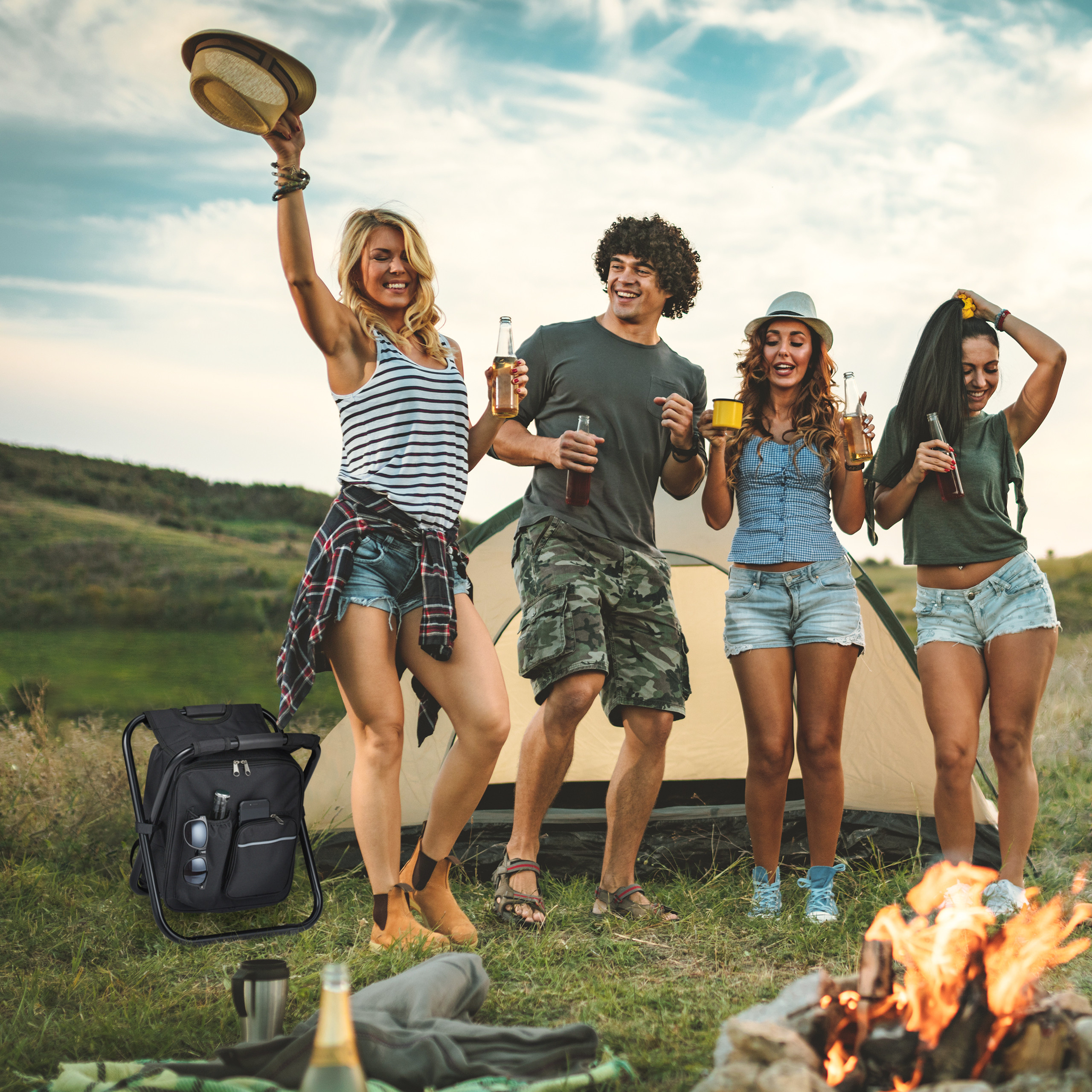Vier Freunde trinken und tanzen bei Sonnenuntergang an einem Zelt und Lagerfeuer.