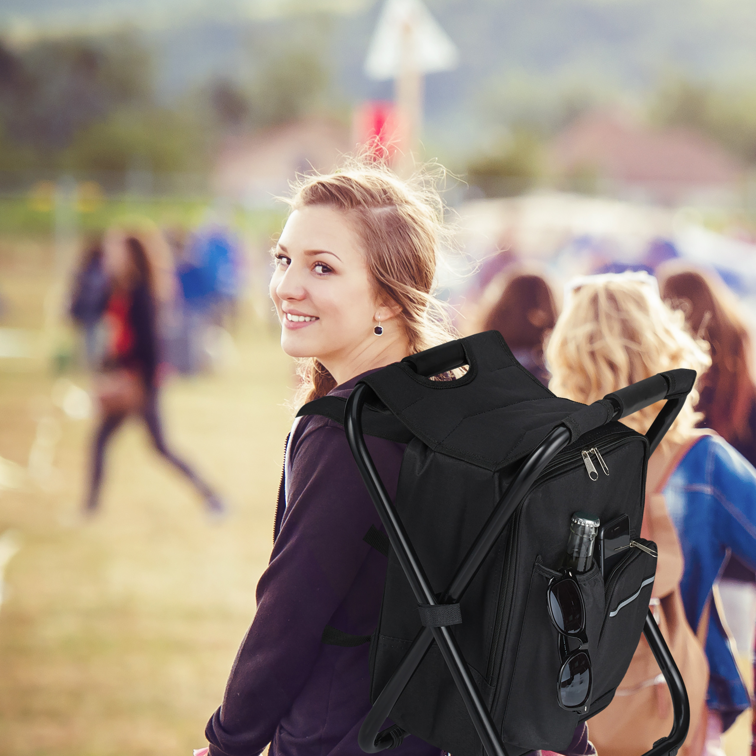 Eine lächelnde junge Frau mit einem schwarzen Rucksack mit integriertem Hocker im Freien, im Hintergrund eine verschwommene Menge.