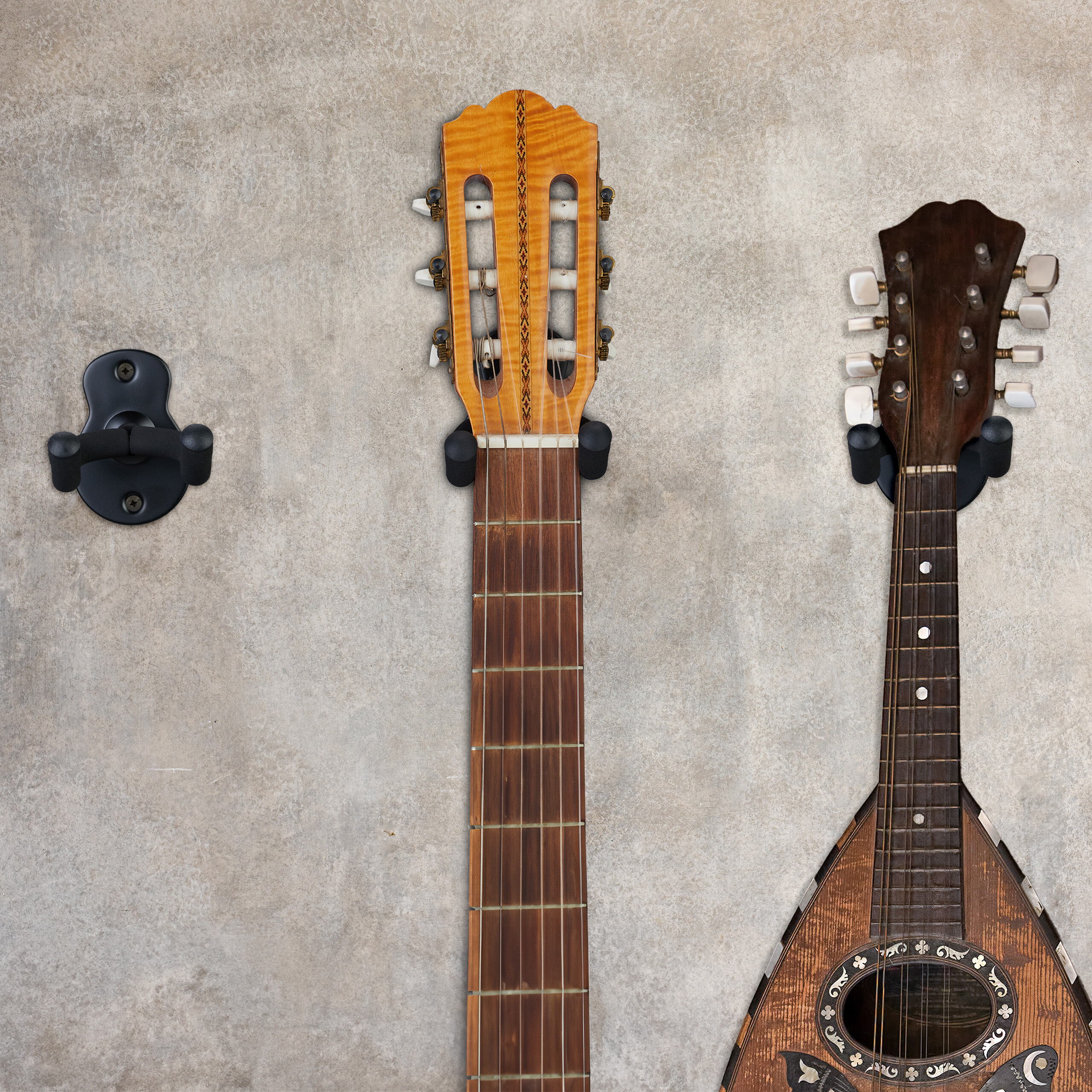 Zwei Saiteninstrumente und eine Gitarrenwandhalterung hängen an einer hellgrauen Betonwand.