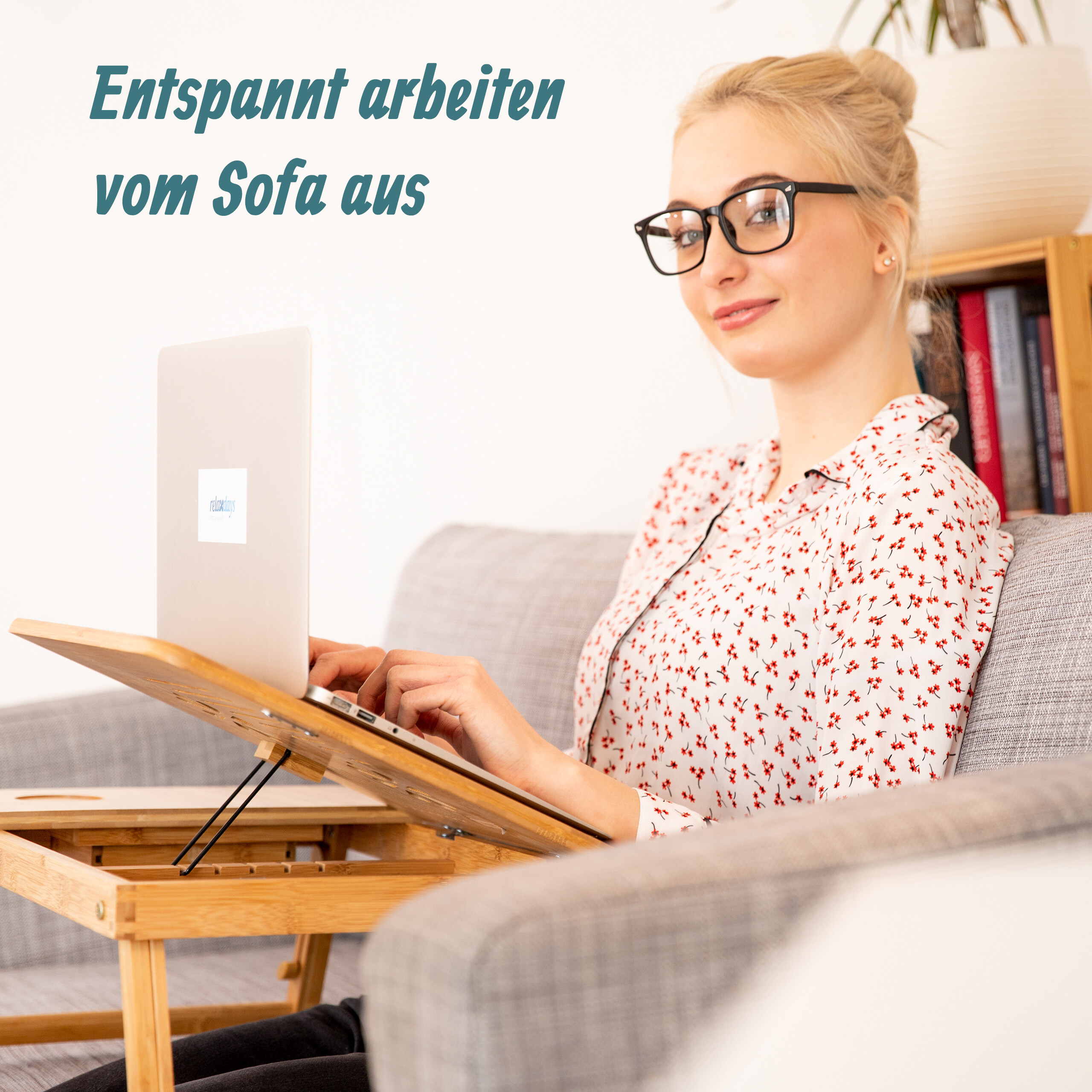 Blonde Frau arbeitet auf einem grauen Sofa mit einem Laptop auf einem Holztisch.