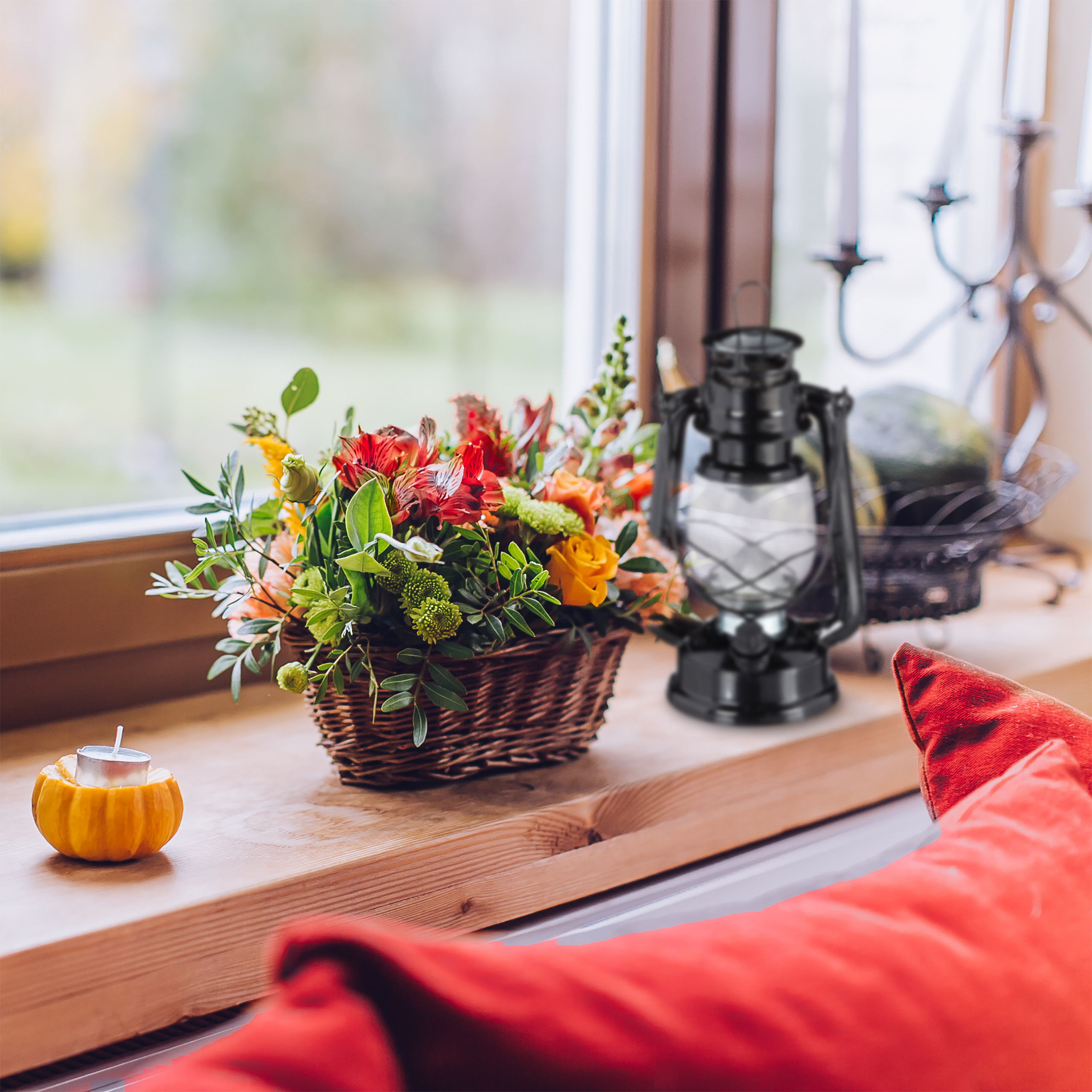 Eine Fensterbank mit Blumenkorb, Laterne, Kürbiskerze und rotem Kissen.