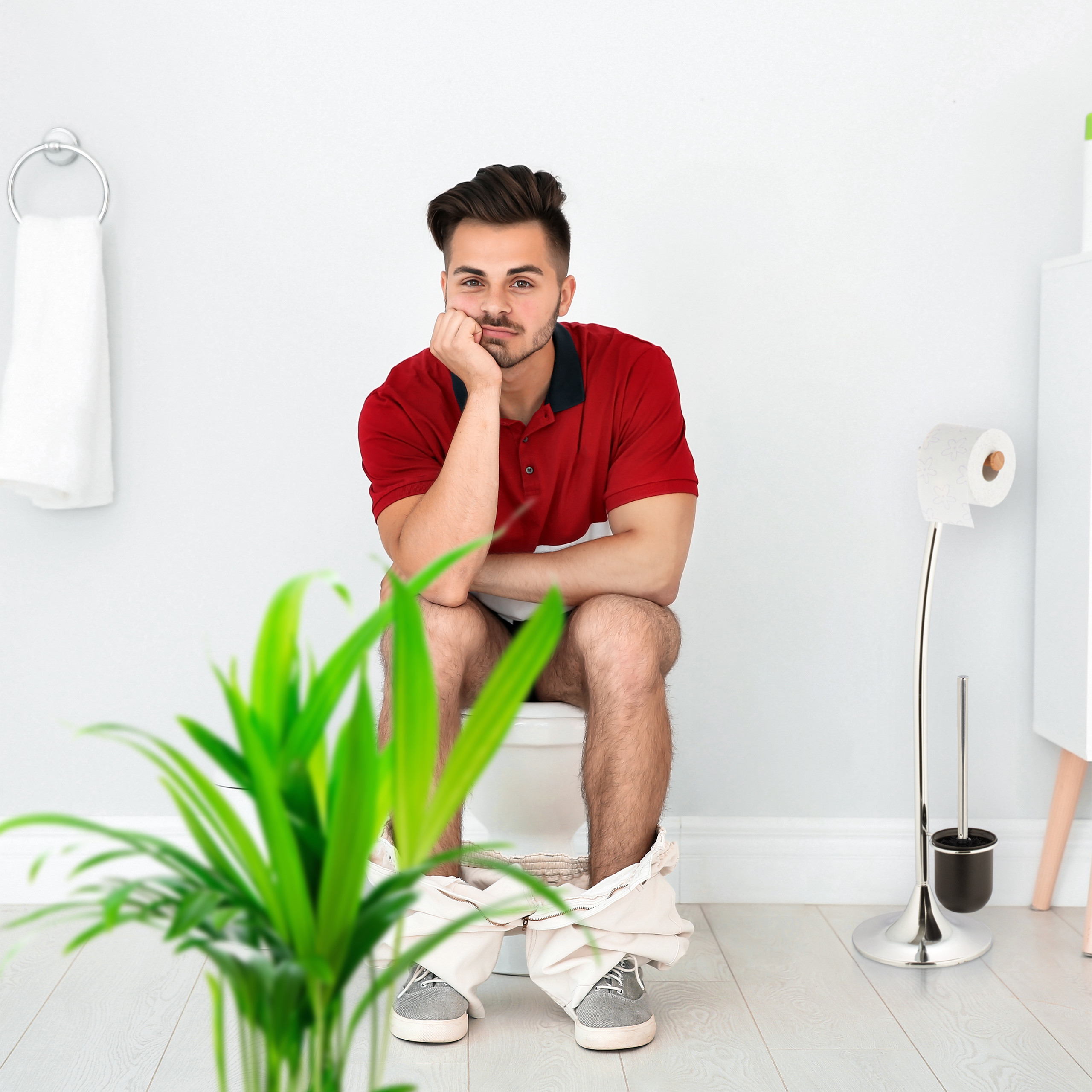 Ein Mann sitzt auf der Toilette, gestützt auf die Hand, in einem weißen Badezimmer.