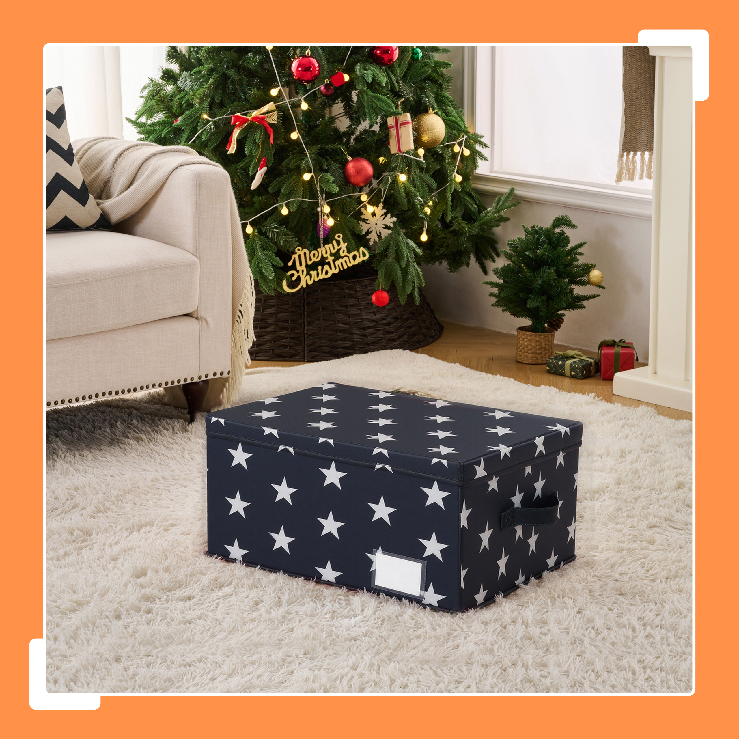 Eine dunkelblaue Aufbewahrungsbox mit weißen Sternen steht vor einem Weihnachtsbaum auf einem hellen Teppich.