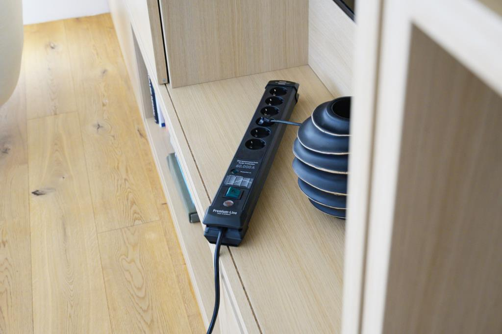 Una ciabatta nera si trova su un ripiano in legno chiaro vicino a un vaso scuro.