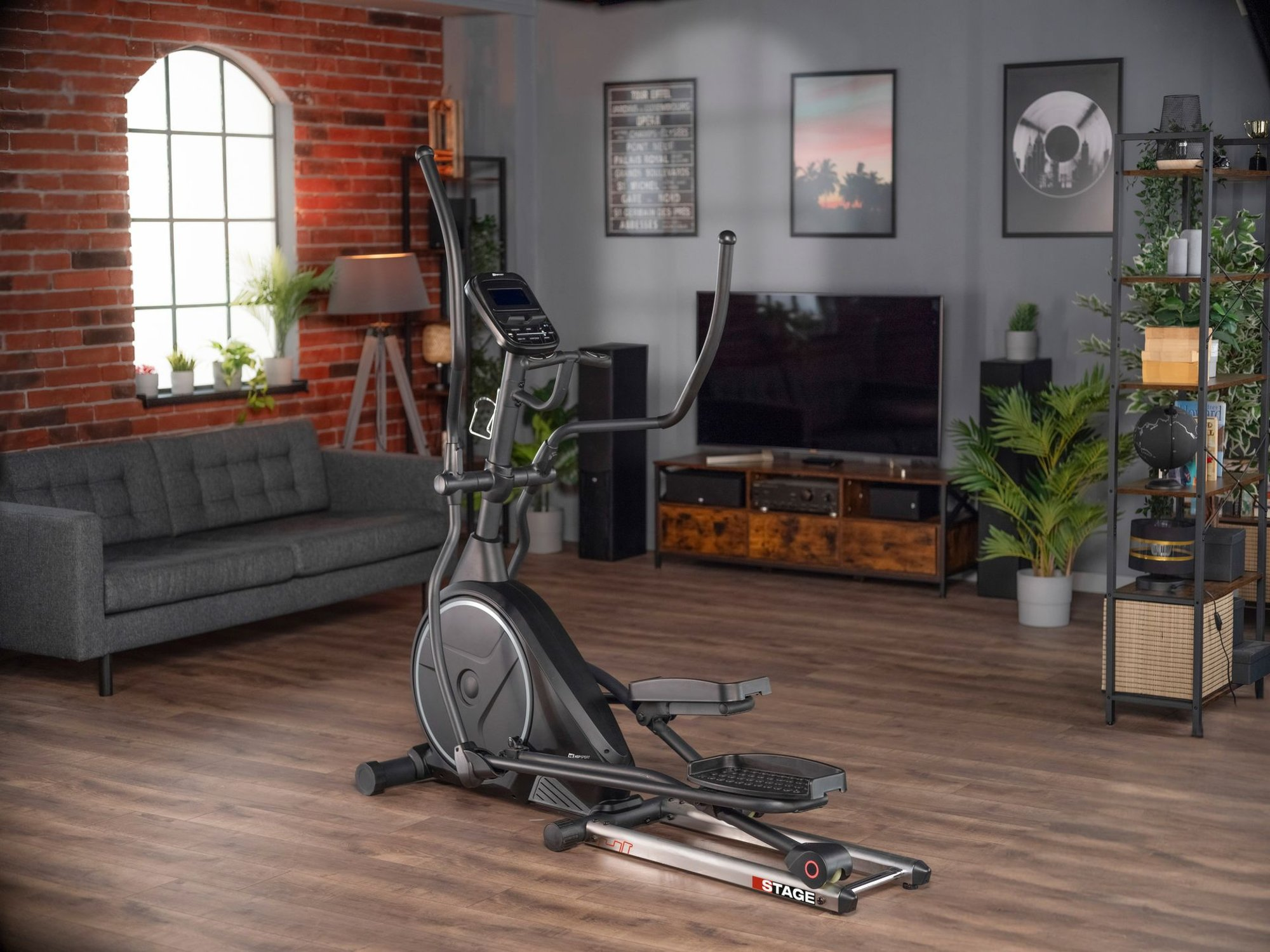 Ein schwarzer Crosstrainer steht in einem modernen Wohnzimmer mit Holzboden, roter Backsteinwand und Pflanzen.