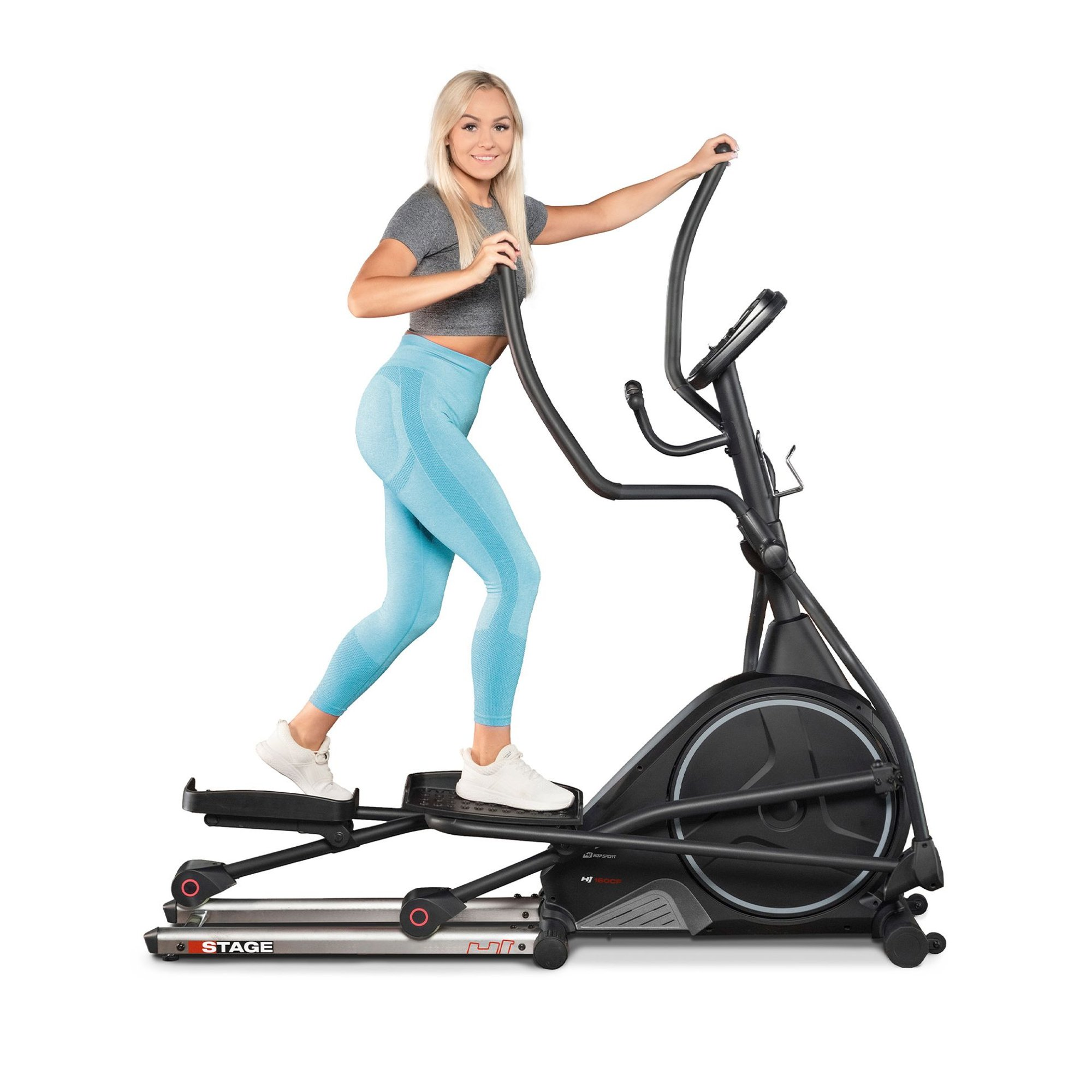 Eine blonde Frau in einem grauen Oberteil und blauen Leggings trainiert auf einem schwarzen Crosstrainer.