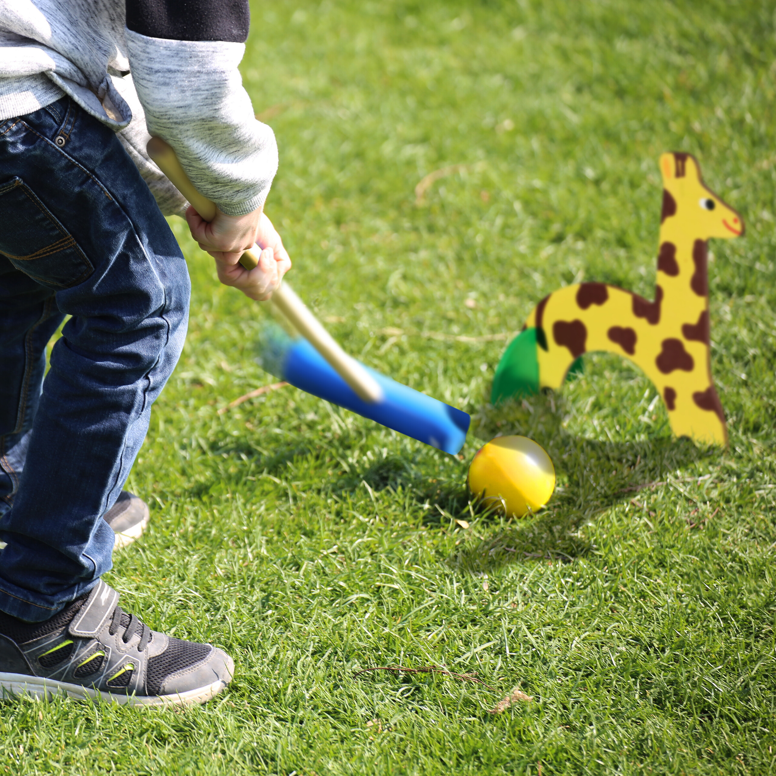 Ein Kind in Jeans spielt Kricket auf dem Rasen und zielt auf ein giraffenförmiges Tor.
