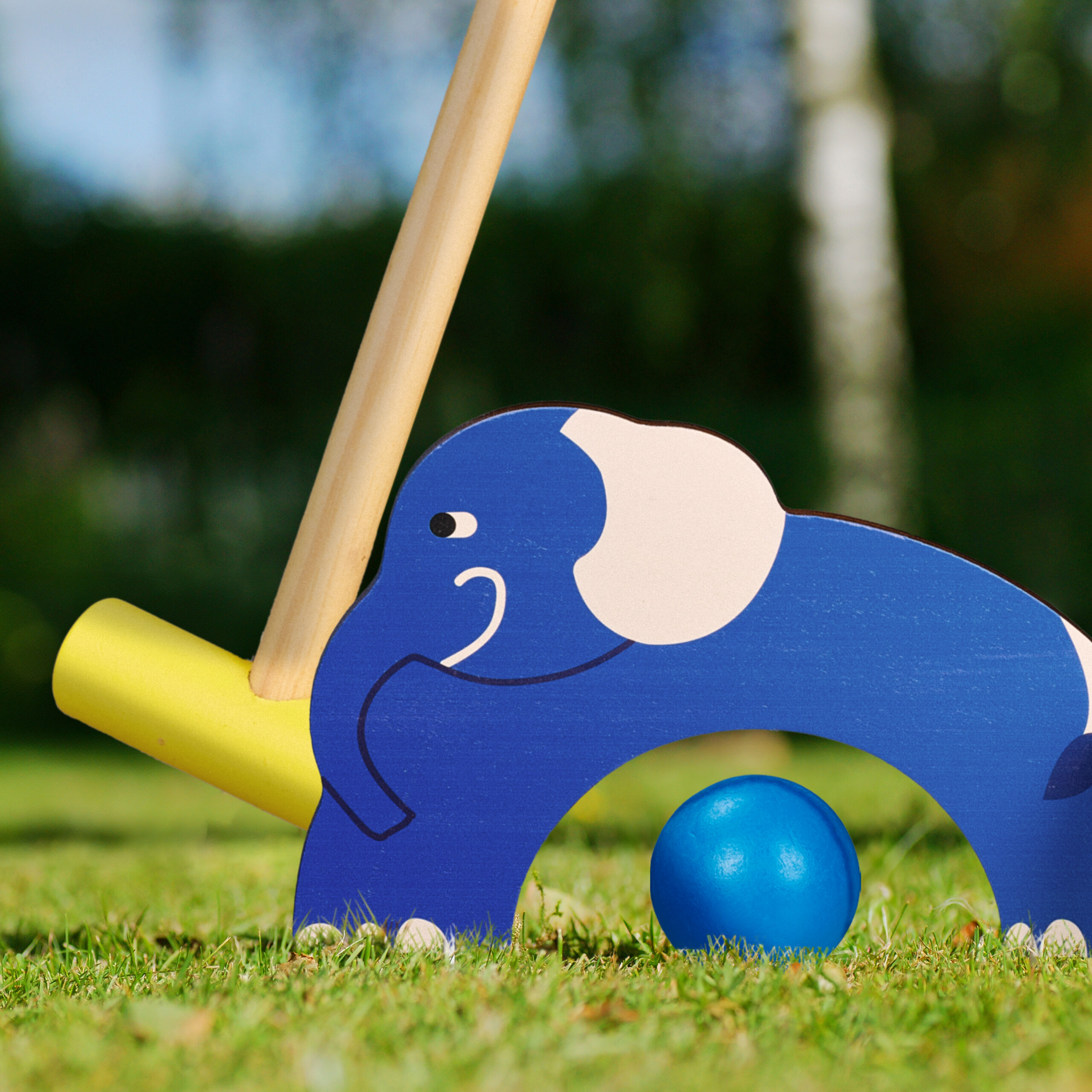 Ein blauer Holzelefant als Hindernis und ein blauer Ball auf Rasen mit einem Krocketmaler.