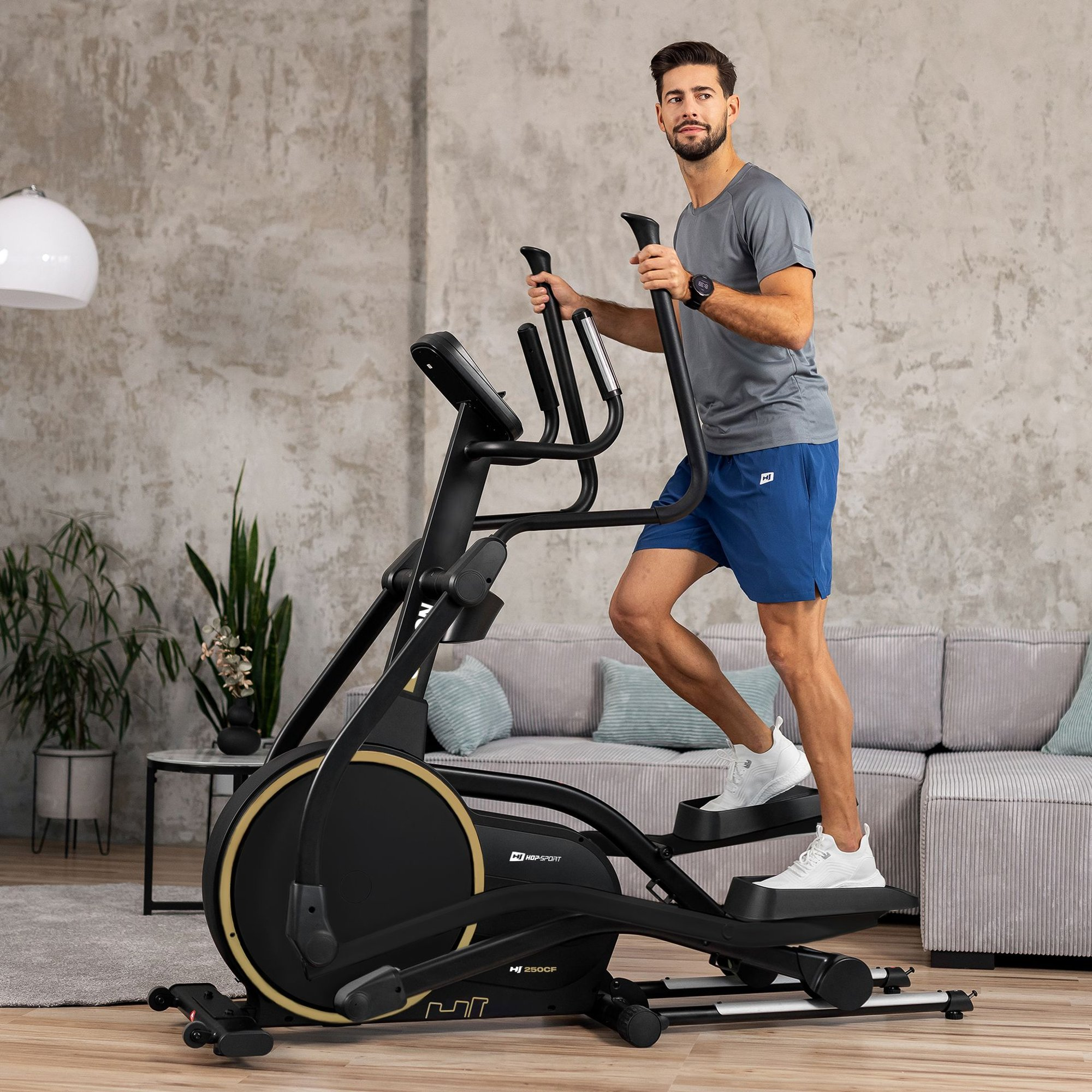 Ein Mann trainiert in einem Wohnzimmer auf einem schwarzen Crosstrainer.