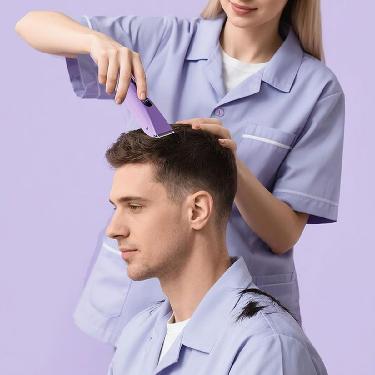 Friseurin schneidet einem Mann mit einer lila Haarschneidemaschine die Haare vor lila Hintergrund.
