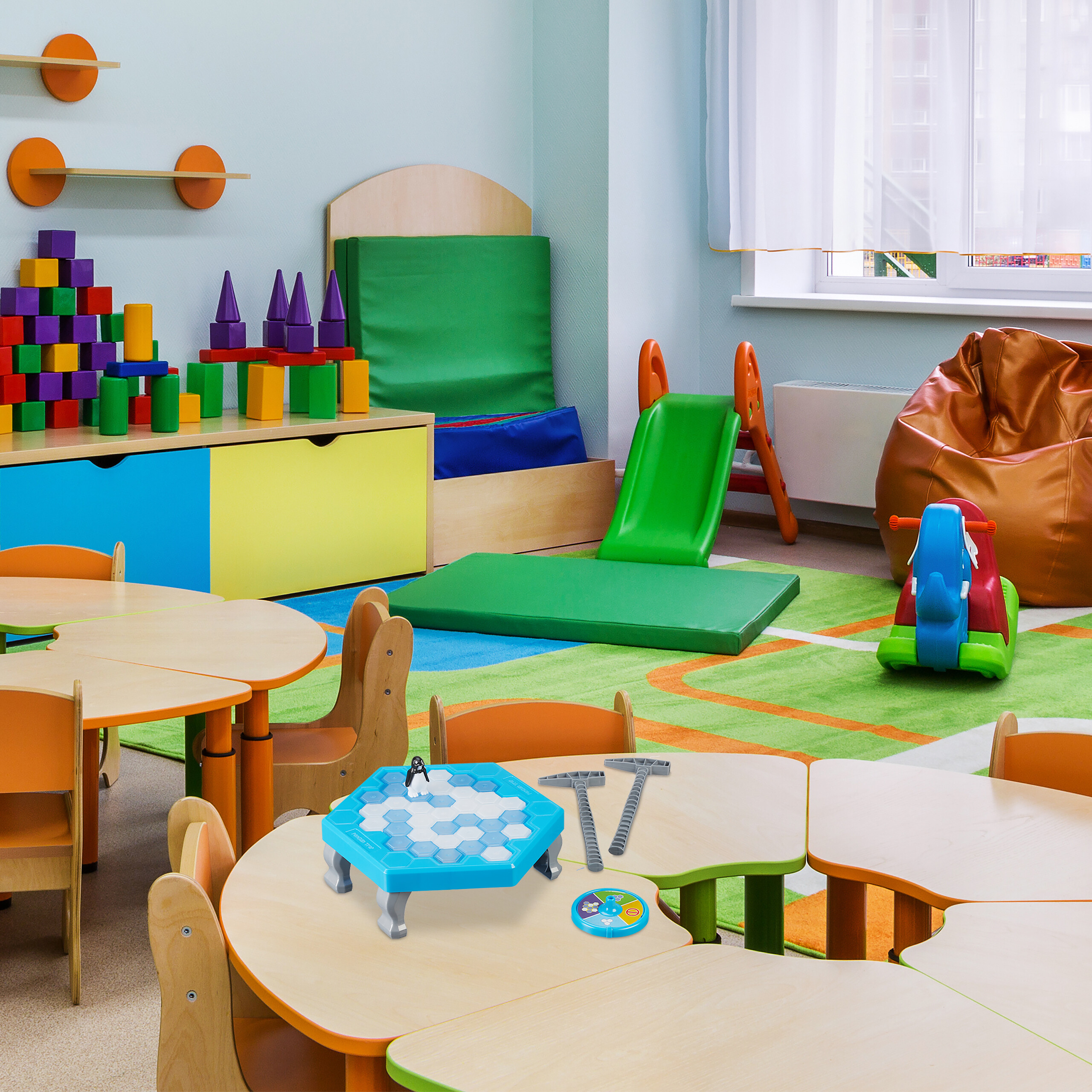 Buntes Kinderspielzimmer mit Tischen, Spielzeug und einer grünen Rutsche.