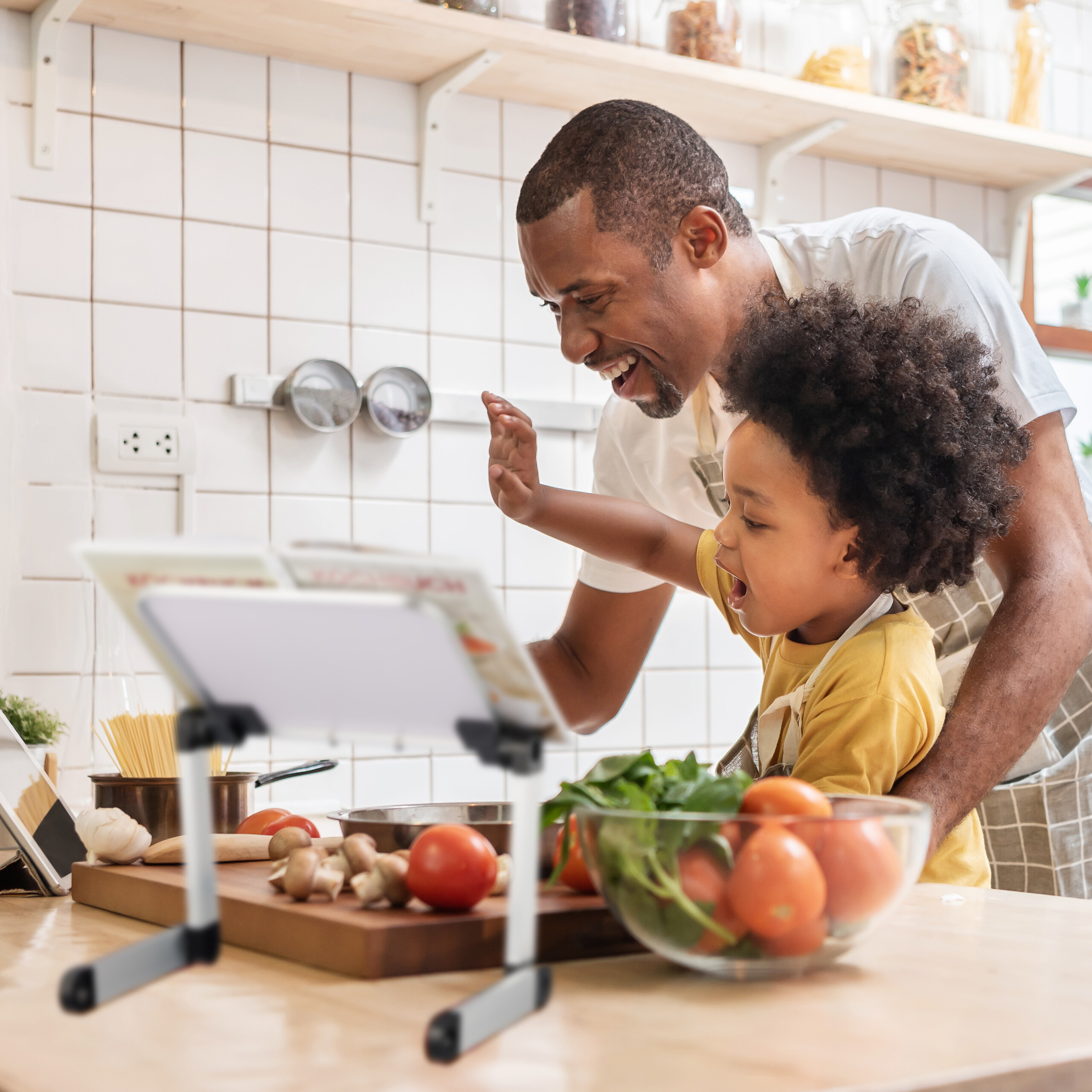 Ein Vater und sein Kind kochen zusammen in der Küche vor einem Tablet.
