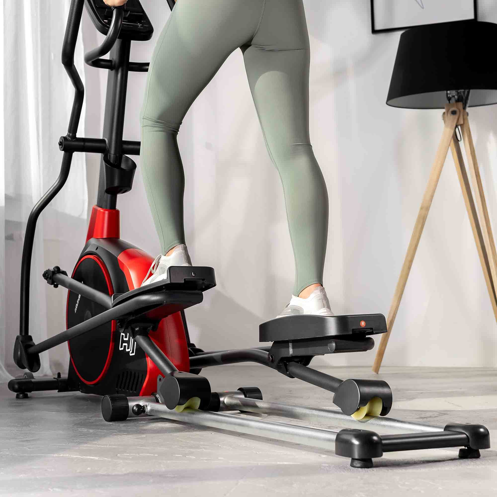 Eine Person trainiert auf einem rot-schwarzen Crosstrainer in einem hellen Raum.