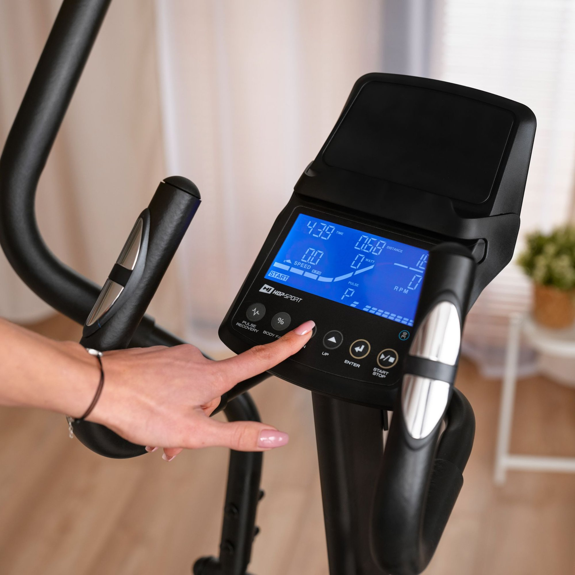 Hand drückt Startknopf auf dem blauen Display eines Crosstrainers.